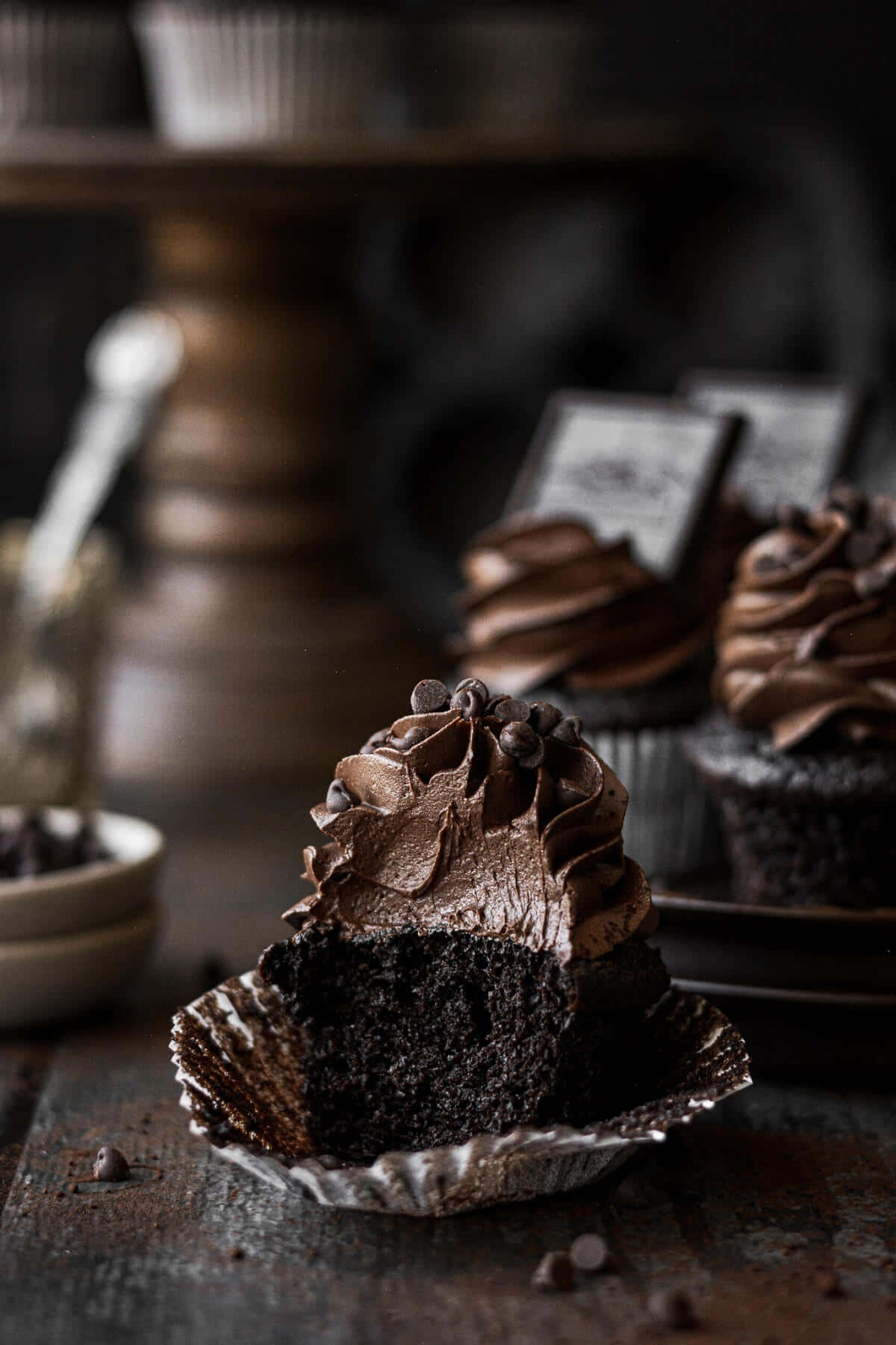 Cupcake 桌布 壁紙 — 一個豐富的巧克力紙杯蛋糕，帶有光澤的糖霜和巧克力片，放在錫箔杯中，置於鄉村風格的木質表面上。