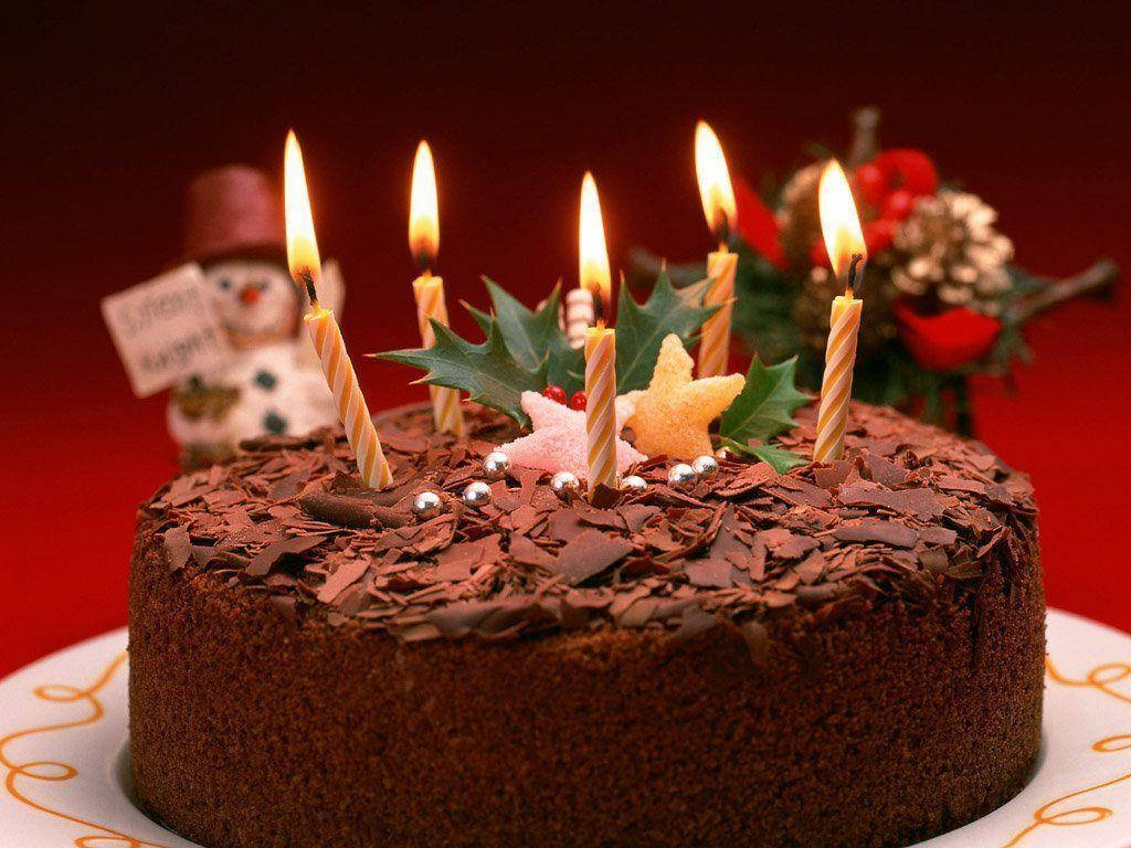 Birthday Cake 桌布 壁紙 — 一個豐富的巧克力蛋糕，上面放著點燃的蠟燭、冬青漿果和一個雪人公仔，背景是深紅色。