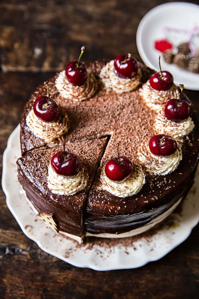 Black Forest Cake 桌布 壁紙 — 一個豐富的巧克力蛋糕，上面有鮮奶油和光澤的櫻桃，放在質樸的木桌上。