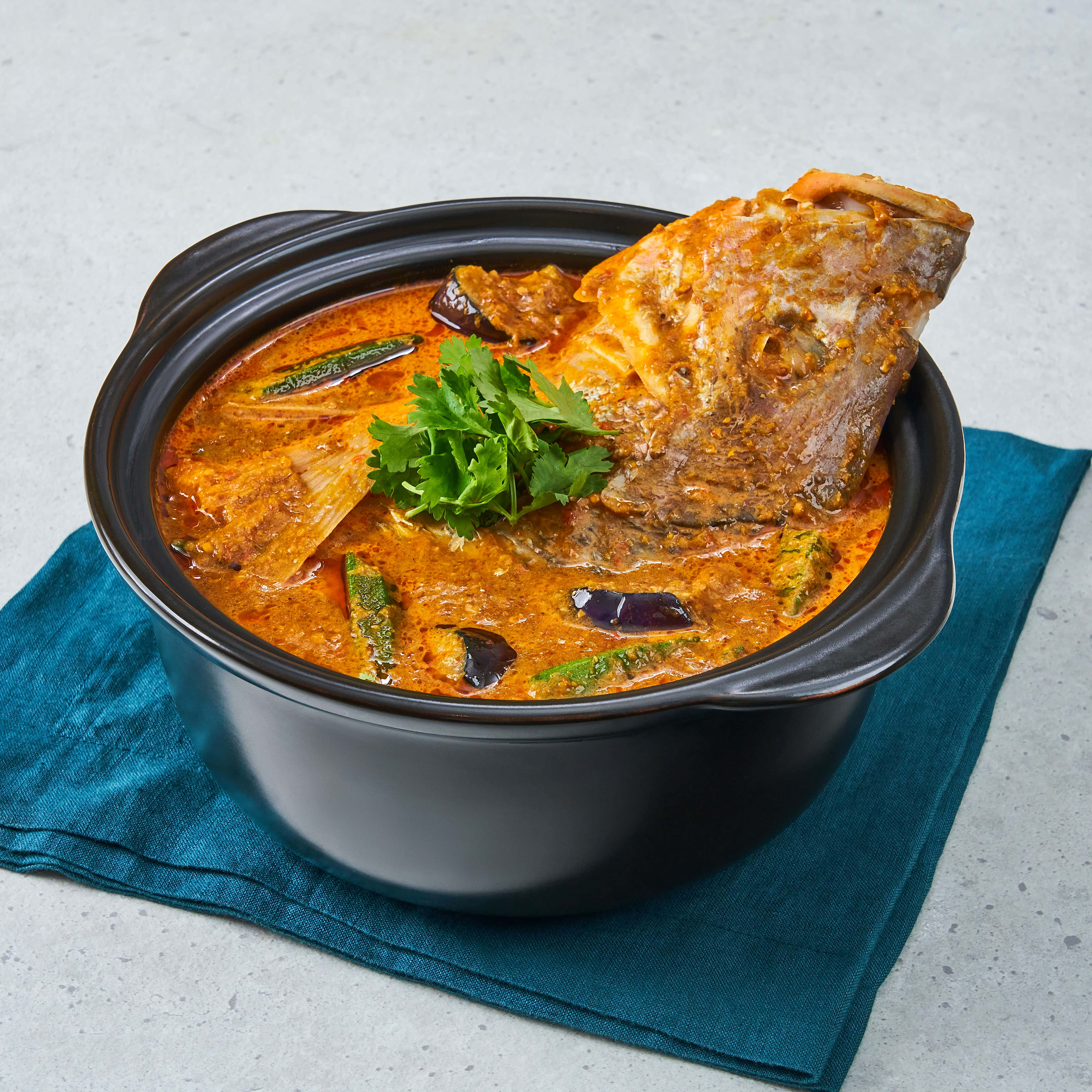 Food Photography 桌布 壁紙 — 一個豐富的橙色魚咖哩，連頭全魚配綠色香草，放在黑色鍋中，置於青綠色餐巾上。