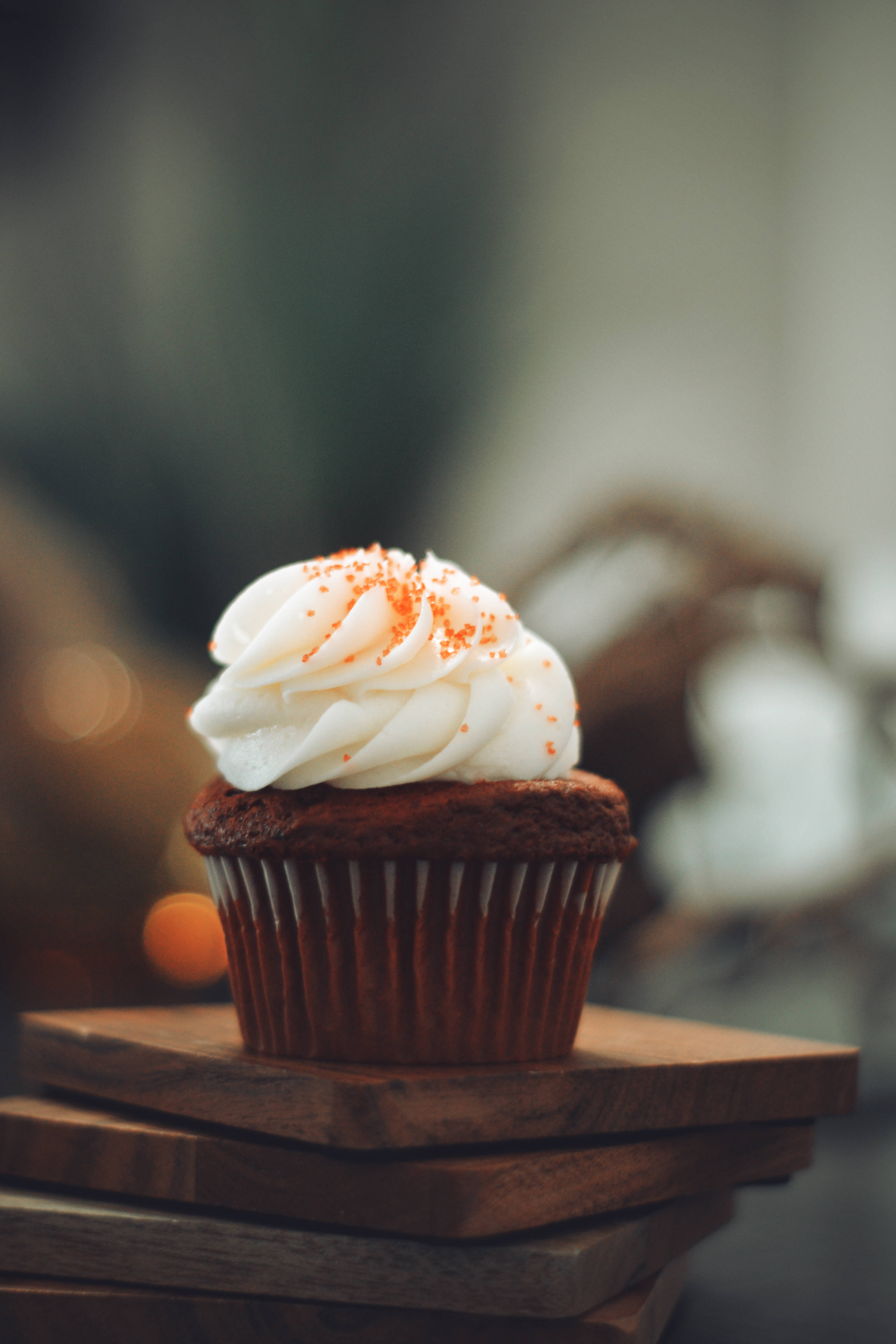 Cupcake 桌布 壁紙 — 一個豐富的紅蘿蔔蛋糕杯子蛋糕，上面有白色糖霜和橙色糖粒的漩渦，放在堆疊的木板上。