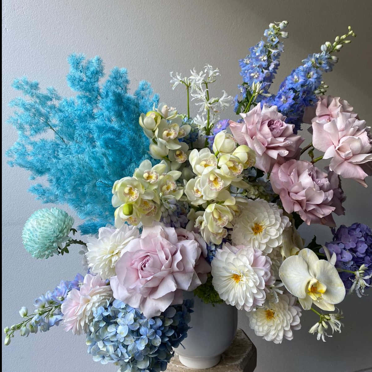 iPhone 桌布 壁紙 — 一個豐富的花卉佈置，採用粉彩粉紅、藍色和白色花朵，放在一個白色花瓶裡，靠著素牆。