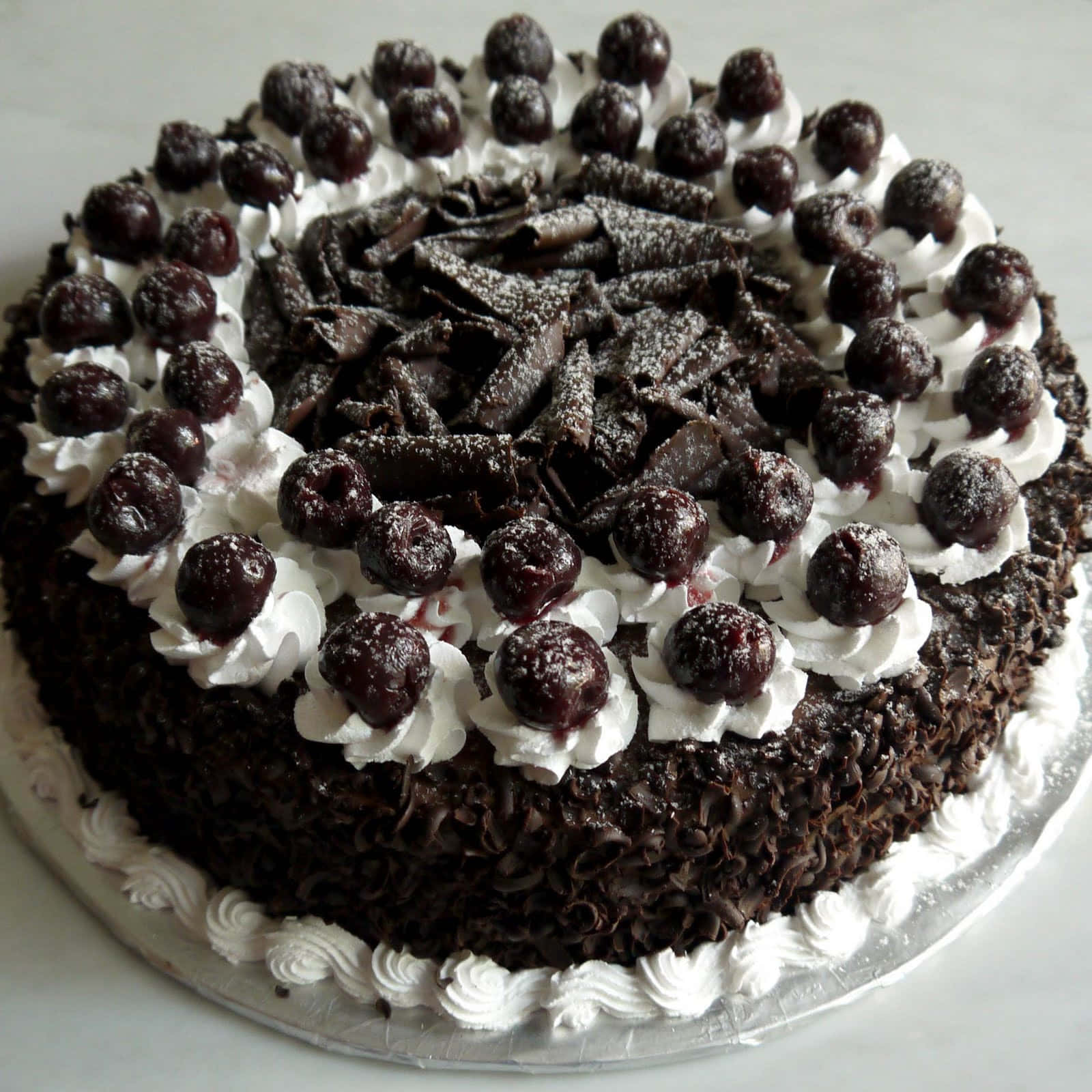 Black Forest Cake 桌布 壁紙 — 一個豐富的黑森林蛋糕，飾以鮮奶油和光澤的櫻桃，優雅地放在銀盤上。