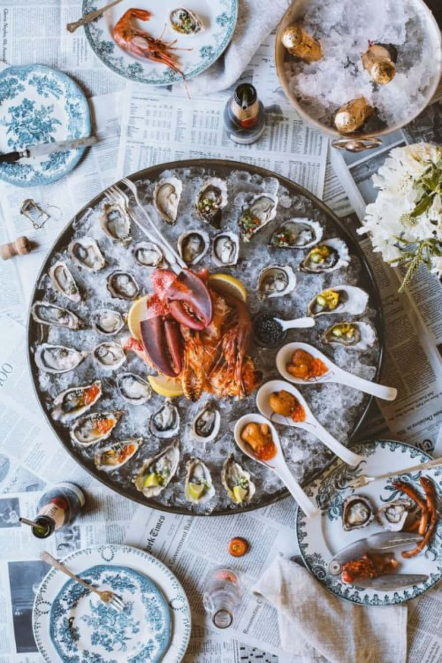 Seafood 桌布 壁紙 — 一個豐盛的海鮮拼盤，以冰上的生蠔和鮮豔的龍蝦為主角，放在鋪滿報紙的桌子上。