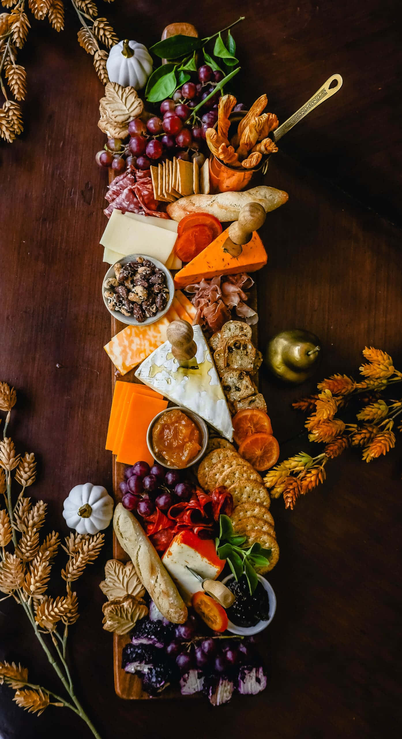 Fall Thanksgiving 桌布 壁紙 — 一個豐盛的秋季熟食拼盤，上面有起司、肉類、葡萄和季節性裝飾，放在深色木桌上。