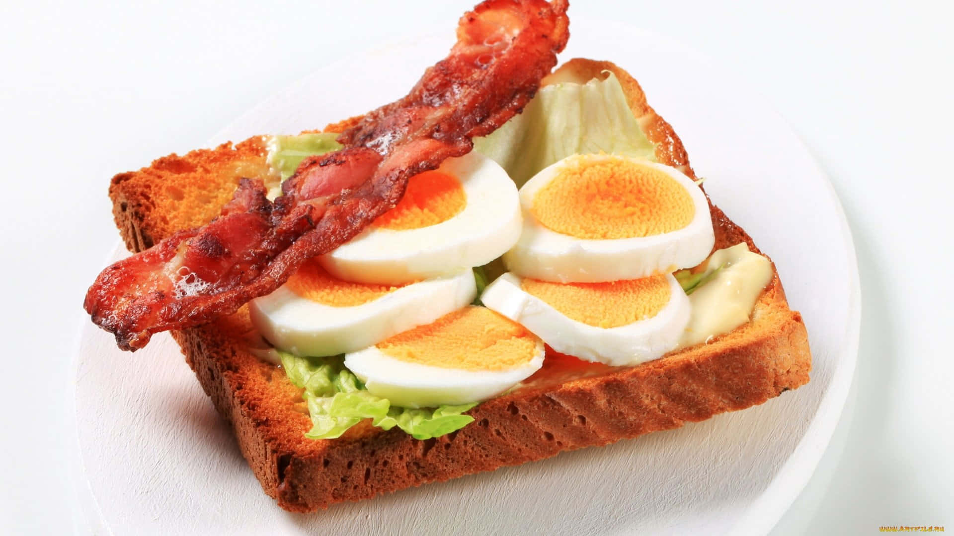 bacon 桌布 壁紙 — 一個豐盛的開放式三明治特寫，上面有脆培根、水煮蛋片和生菜，放在烤吐司上。