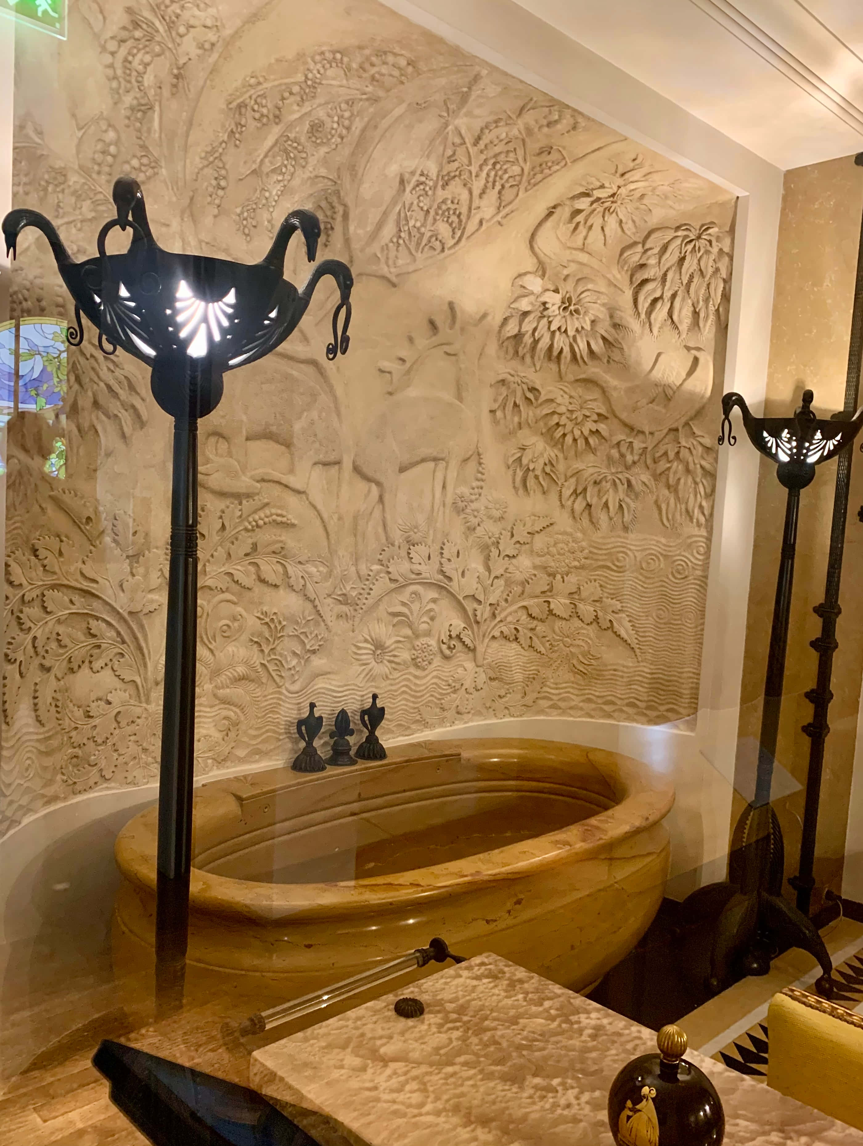 Bathtub 桌布 壁紙 — 一個豪華大理石浴缸位於精雕細琢的鹿與樹葉牆壁浮雕下方，兩側是華麗的黑色燈具。
