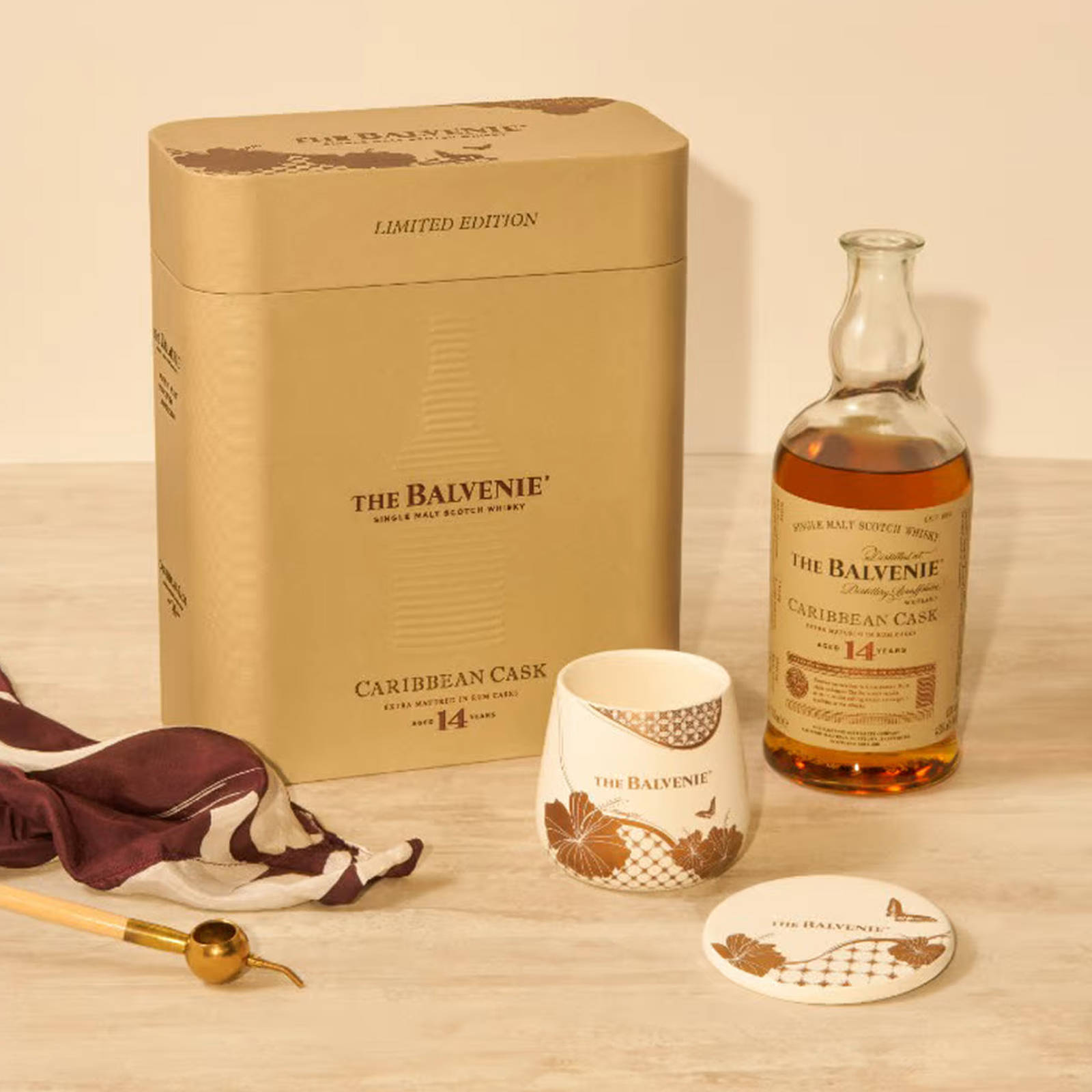 Drink 桌布 壁紙 — 一個豪華的 Balvenie 威士忌套裝，包括金色包裝、琥珀色瓶子和圖案杯子，擺放在淺色木質表面上。