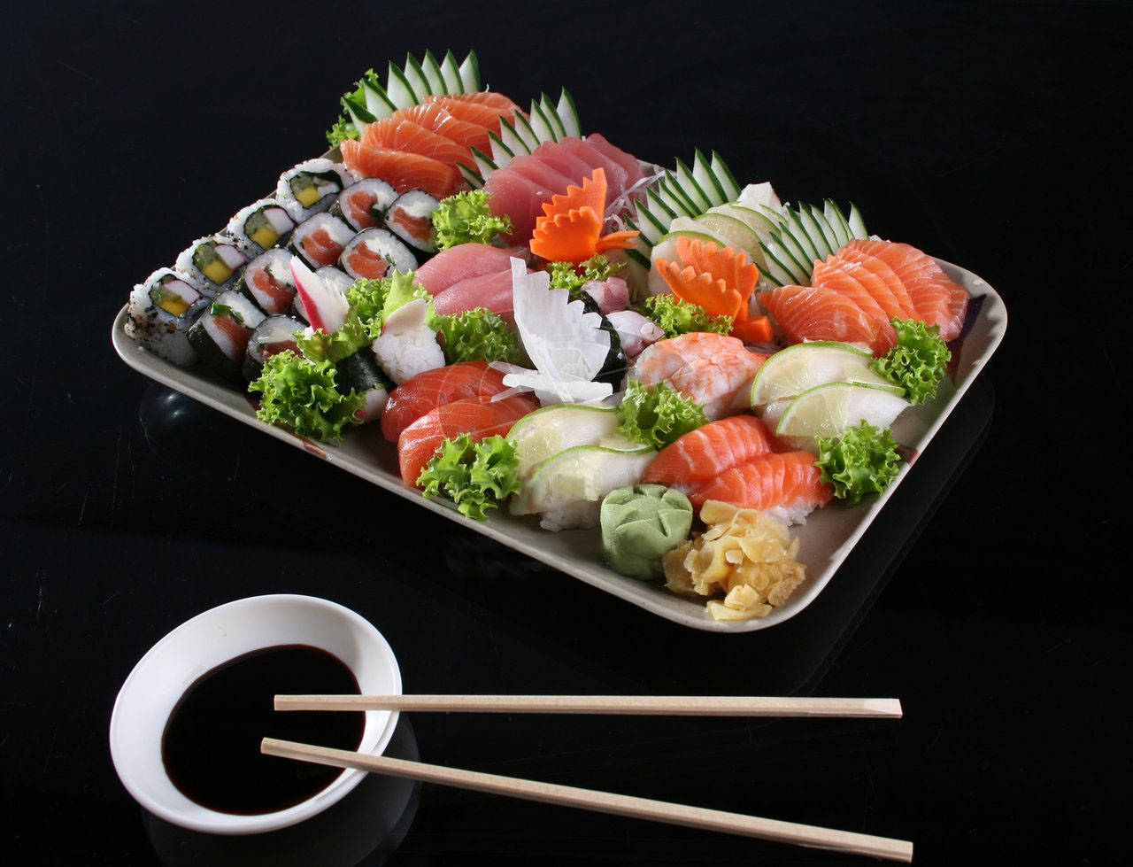 Salmon 桌布 壁紙 — 一個豪華的壽司和刺身拼盤，在黑表面上藝術地擺放著裝飾和芥末，配以醬油和筷子。