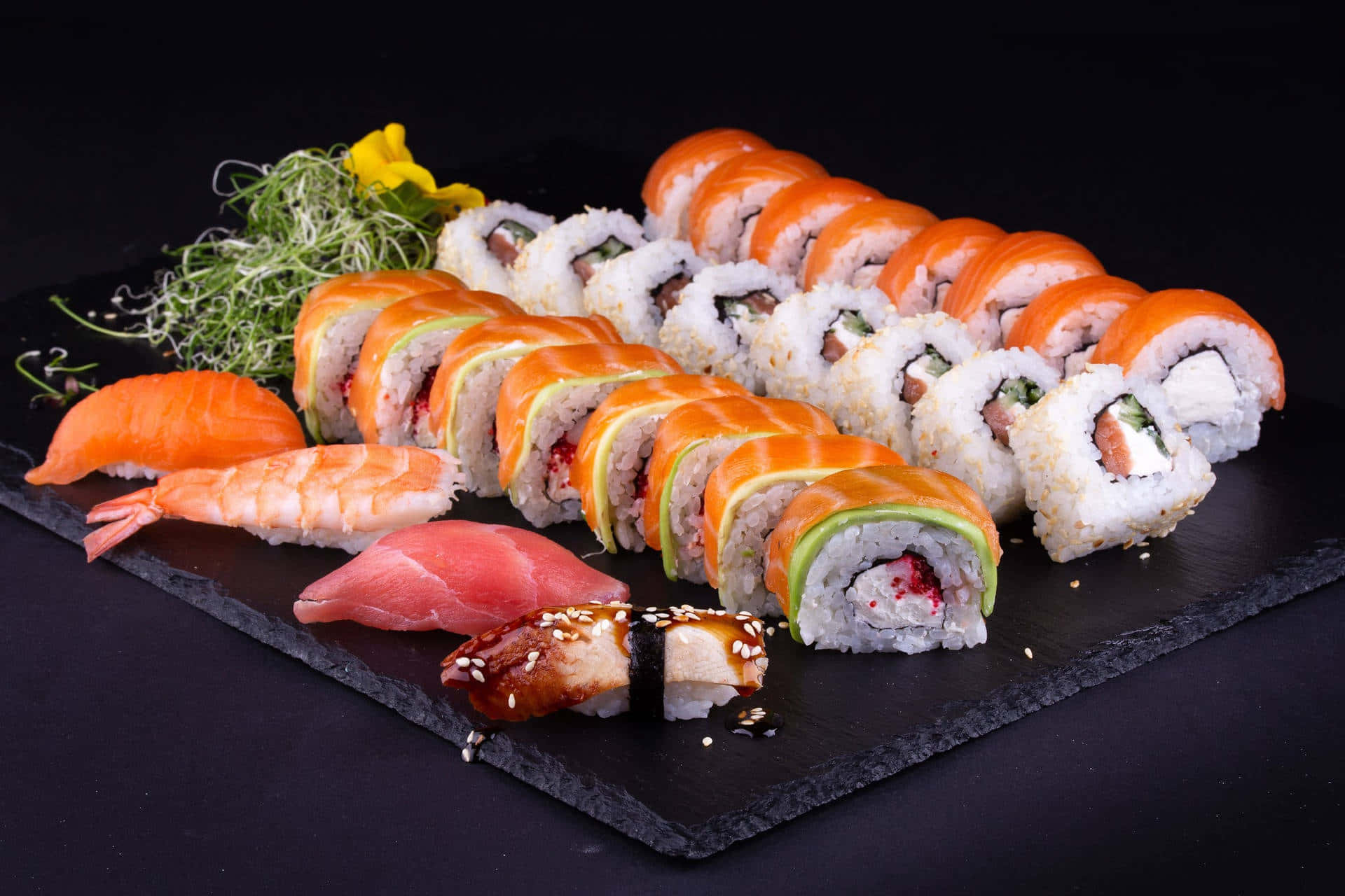 Sushi 桌布 壁紙 — 一個豪華的壽司拼盤，包括鮭魚卷、鮪魚握壽司、蝦天婦羅和配菜，放在黑色石板上的深色背景中。