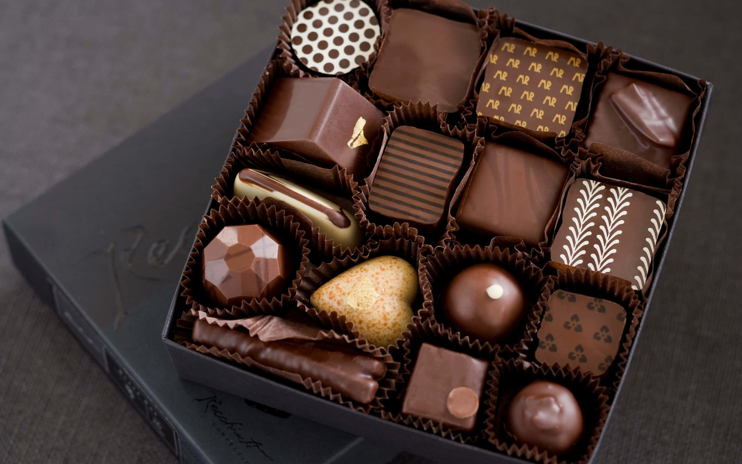 Chocolate 桌布 壁紙 — 一個豪華的打開盒子，裡面裝有各種精緻美食巧克力，設計精巧，質感豐富。