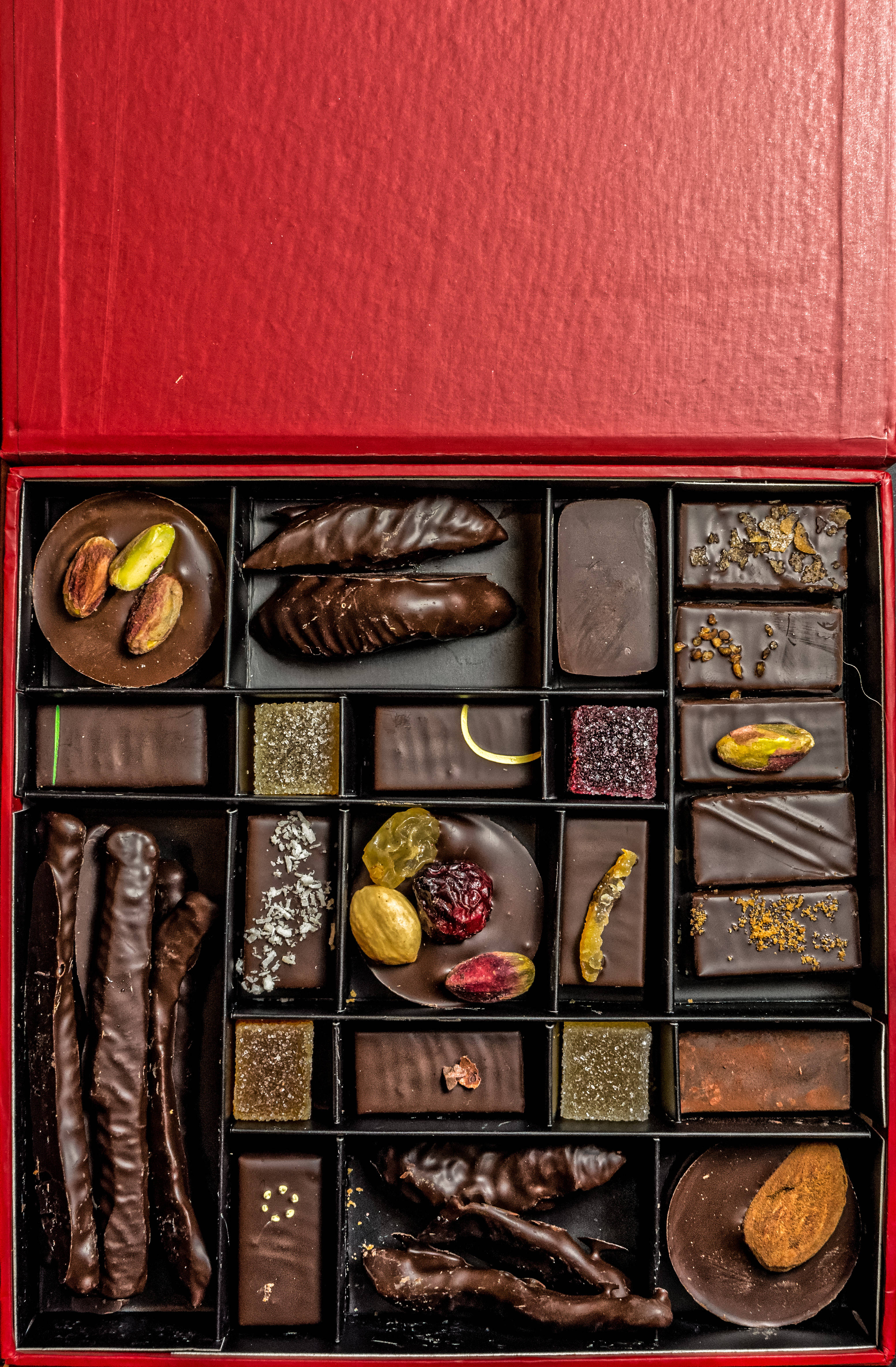 Chocolate 桌布 壁紙 — 一個豪華的紅色盒子，裡面裝滿了各種美食巧克力，包括開心果、乾果和堅果，包裹在濃郁的黑巧克力中。