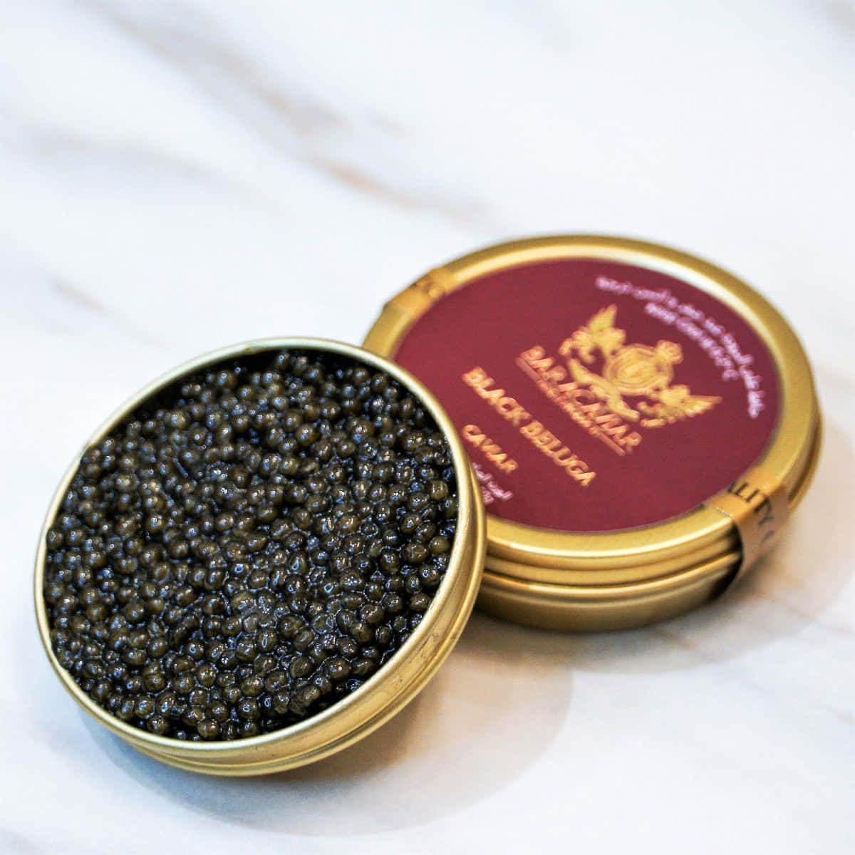 Black Caviar 桌布 壁紙 — 一個豪華的開放式黑鱘魚子醬罐頭放在白色大理石表面上，金色蓋子在旁邊。