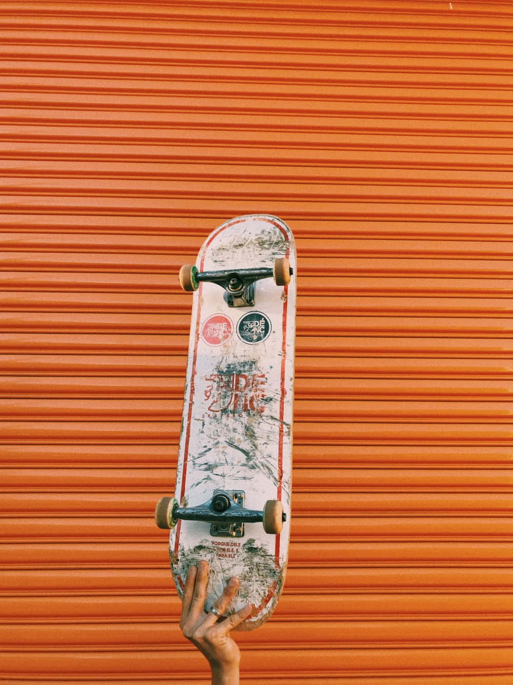 Retro Skateboard 桌布 壁紙 — 一個貼有貼紙的舊滑板垂直靠在鮮橙色波紋金屬牆上。