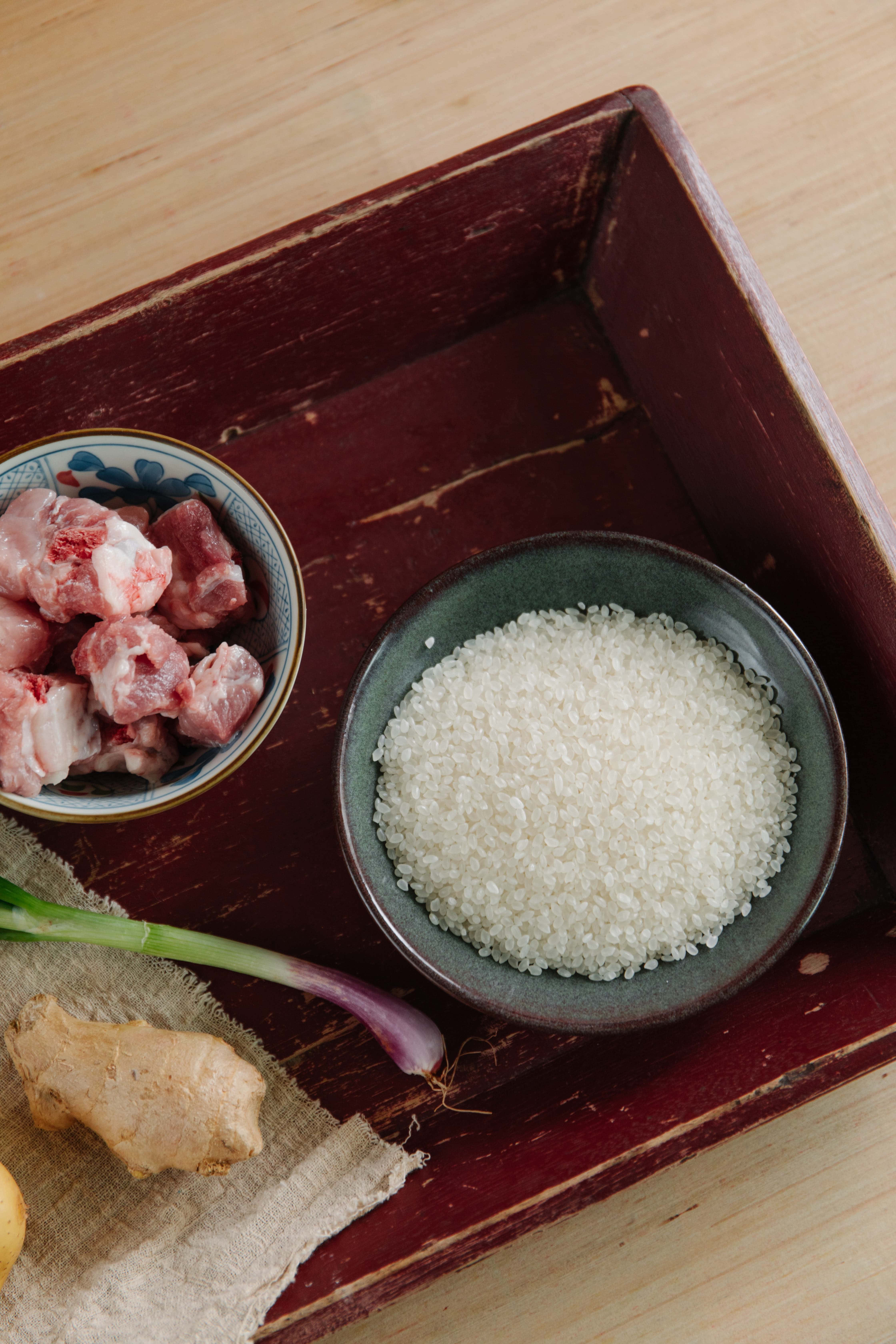 Rice 桌布 壁紙 — 一個質樸的木托盤上放著碗裝的生豬肋骨、白米和新鮮生薑，用於傳統亞洲餐點準備。