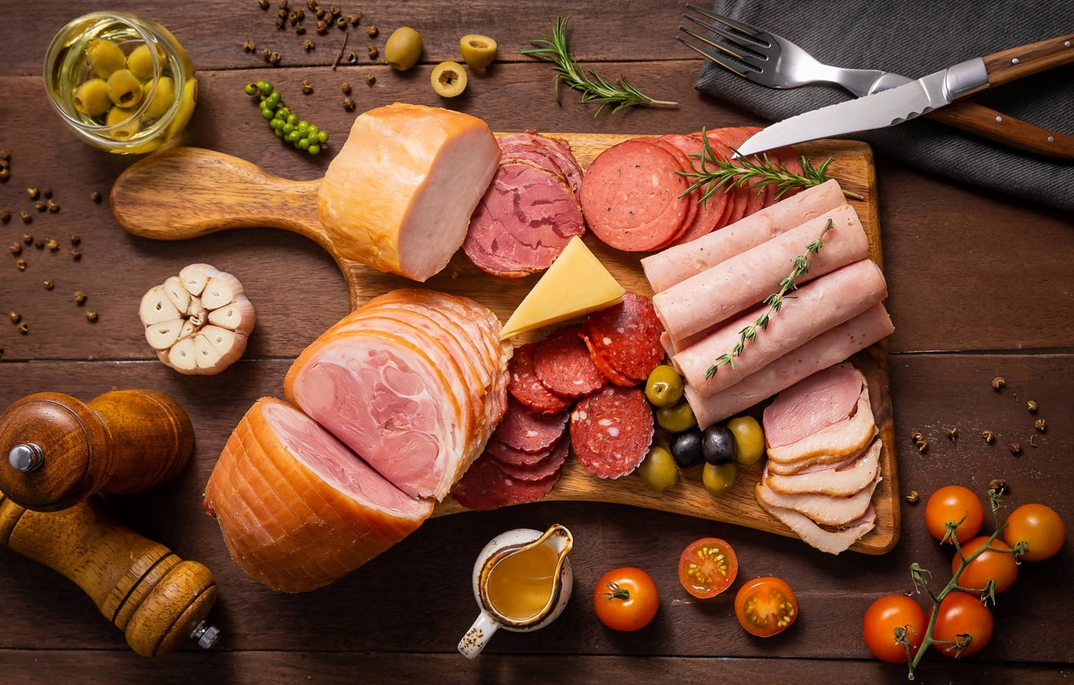 Ham 桌布 壁紙 — 一個質樸的木板上擺滿了切片醃肉、起司、橄欖、番茄和新鮮香草，放在深色木桌上。