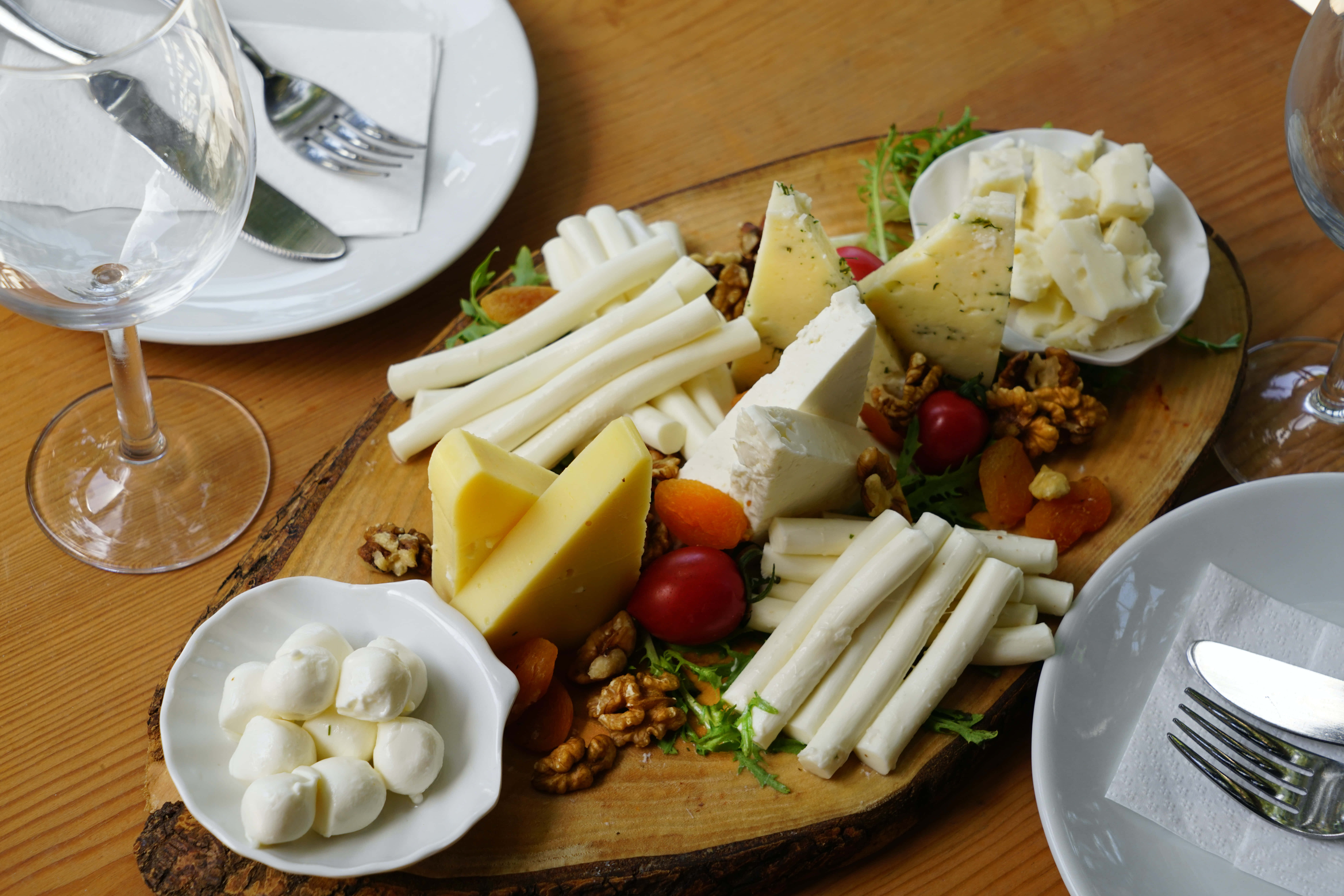 Cheese 桌布 壁紙 — 一個質樸的木板上放滿了各式各樣的起司、堅果和櫻桃番茄，放在溫暖的木桌上，旁邊有酒杯。