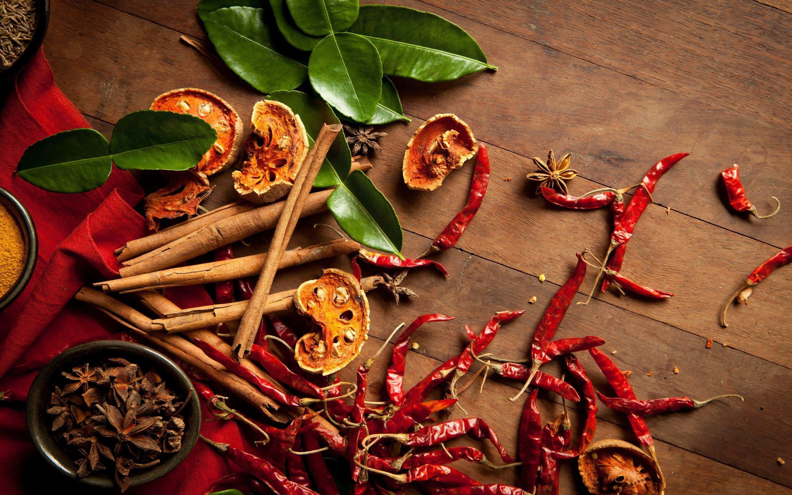 Spices 桌布 壁紙 — 一個質樸的木桌上展示了鮮紅色的辣椒、肉桂棒、八角、乾柑橘片和新鮮綠葉。