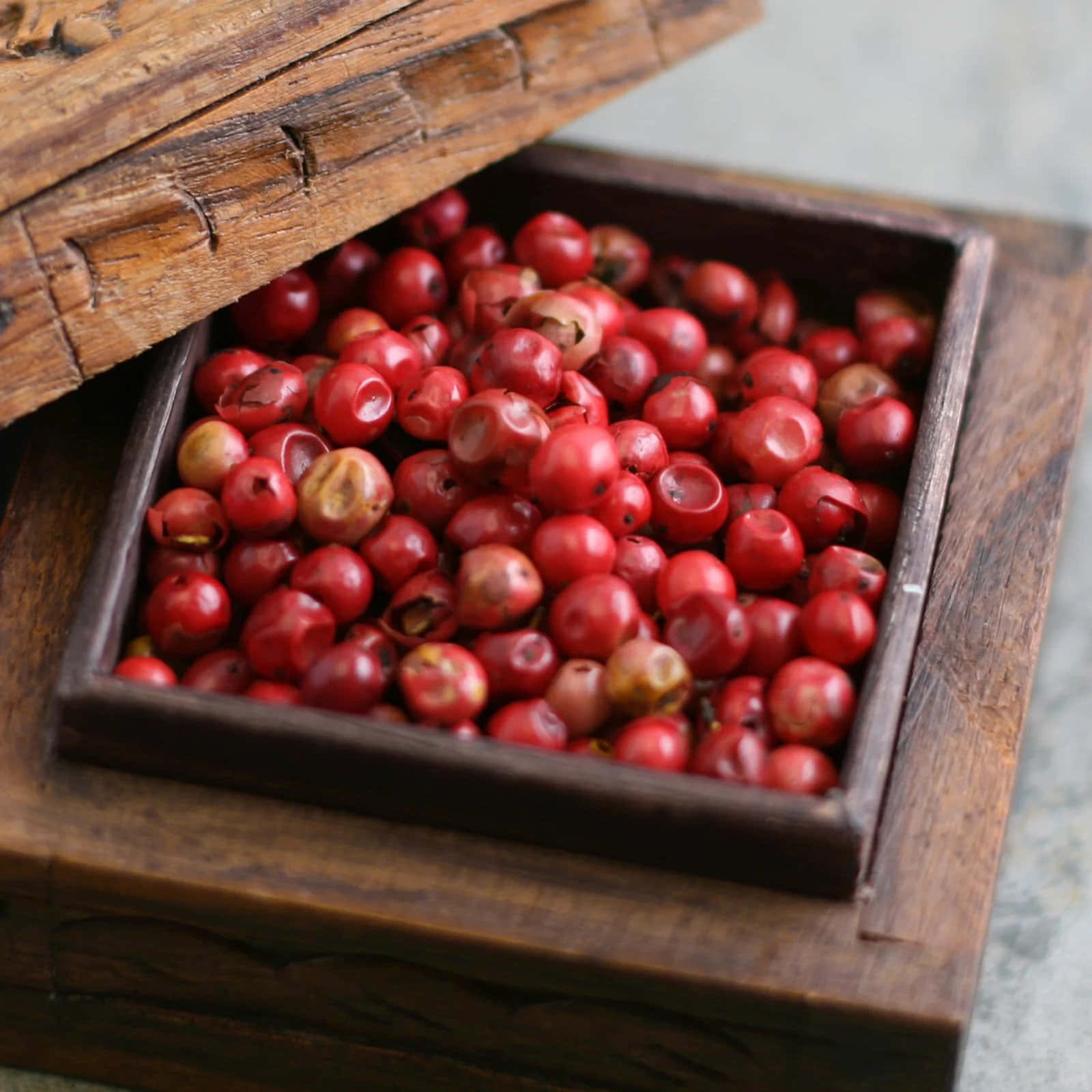 Pink Peppercorn 桌布 壁紙 — 一個質樸的木箱，裝滿鮮紅的胡椒粒，展現豐富的質感和溫暖色調。
