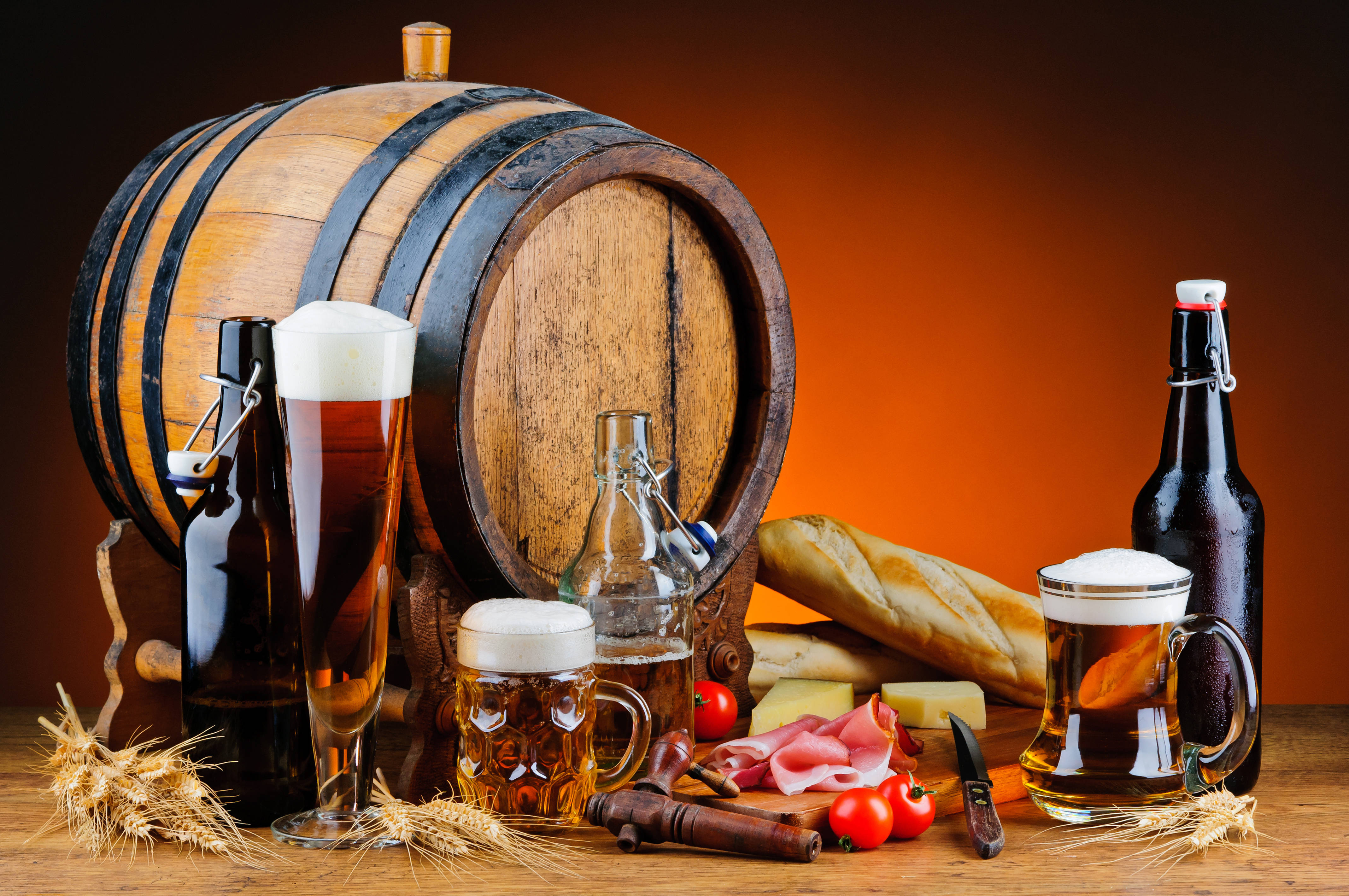 Beer 桌布 壁紙 — 一個質樸的木製啤酒桶，周圍環繞著玻璃杯、瓶子和食物，放在溫暖的木桌上。