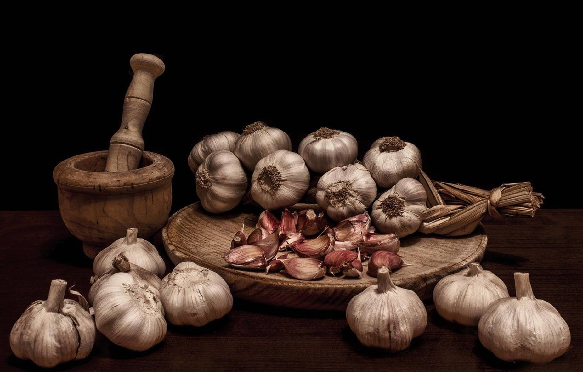 Garlic 桌布 壁紙 — 一個質樸的木製研缽和研杵放在一個盛滿完整和去皮蒜瓣的碗旁邊，背景為深色。