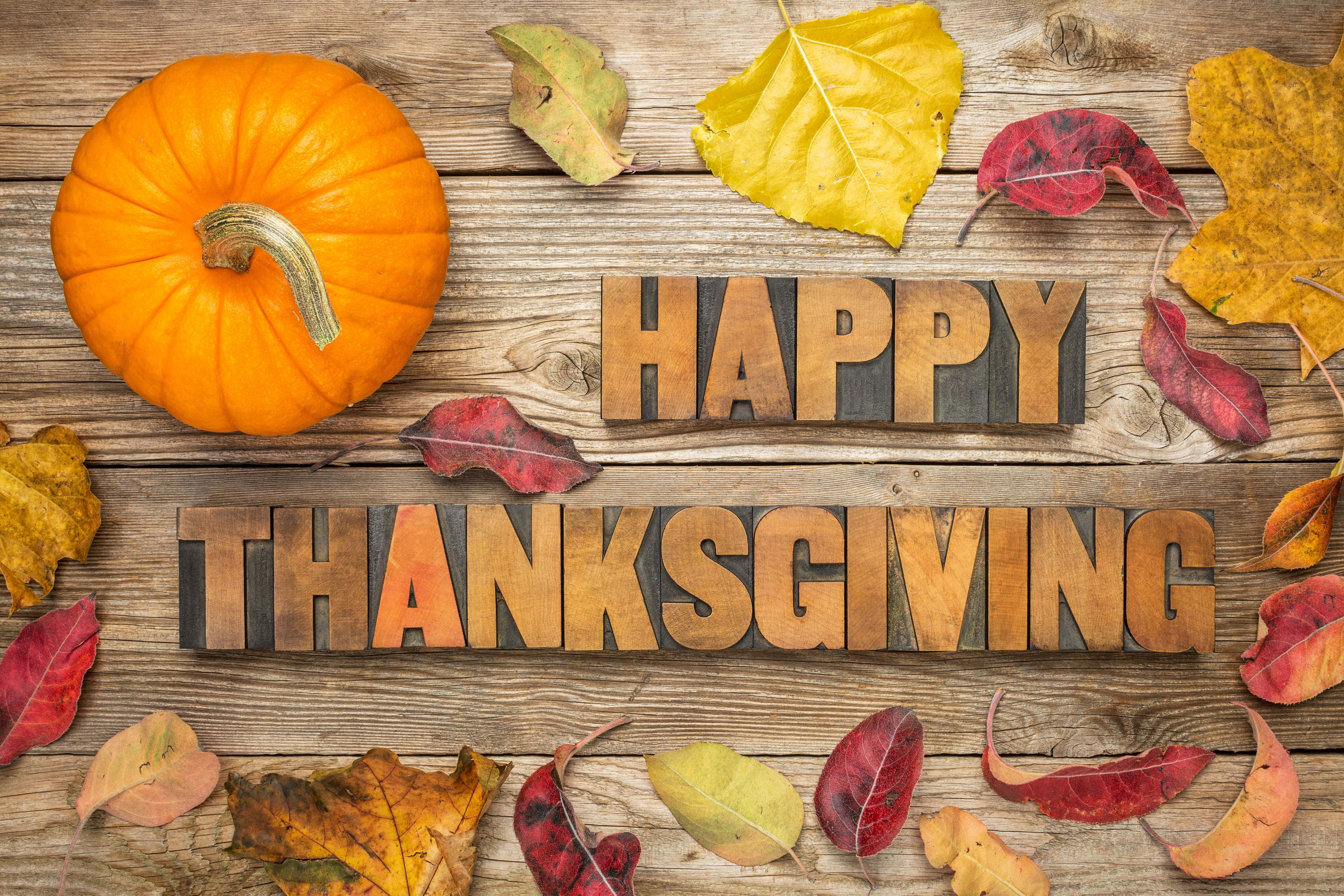 Happy Thanksgiving 桌布 壁紙 — 一個質樸的木質表面上，裝飾著一個鮮橙色的南瓜和色彩繽紛的秋葉，周圍環繞著復古木活字塊，拼出「HAPPY THANKSGIVING」。