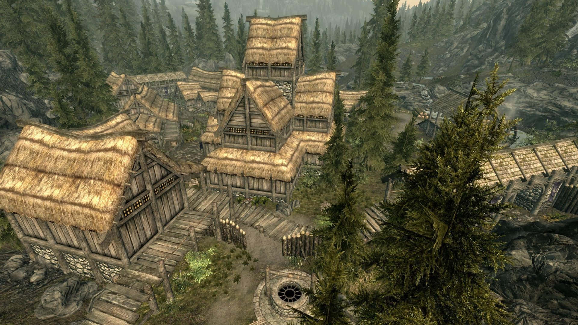 Skyrim Falkreath 桌布 壁紙 — 一個質樸的木造村莊，茅草屋頂，坐落在霧氣瀰漫的山谷中，四周是高聳的松樹。