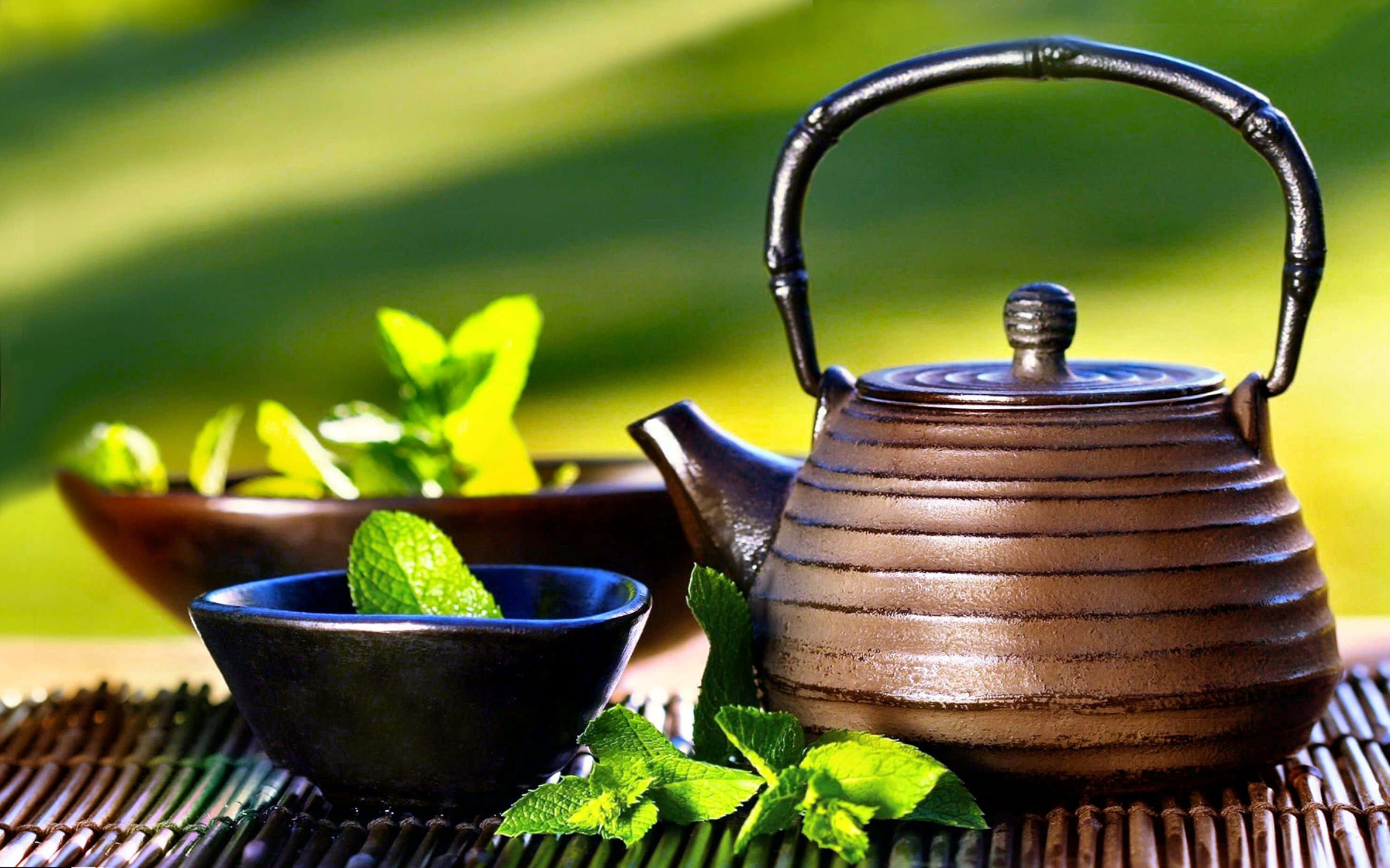 tea 桌布 壁紙 — 一個質樸的棕色陶瓷茶壺和碗，搭配新鮮薄荷葉，放在編織墊上，背景是充滿活力的模糊綠色。