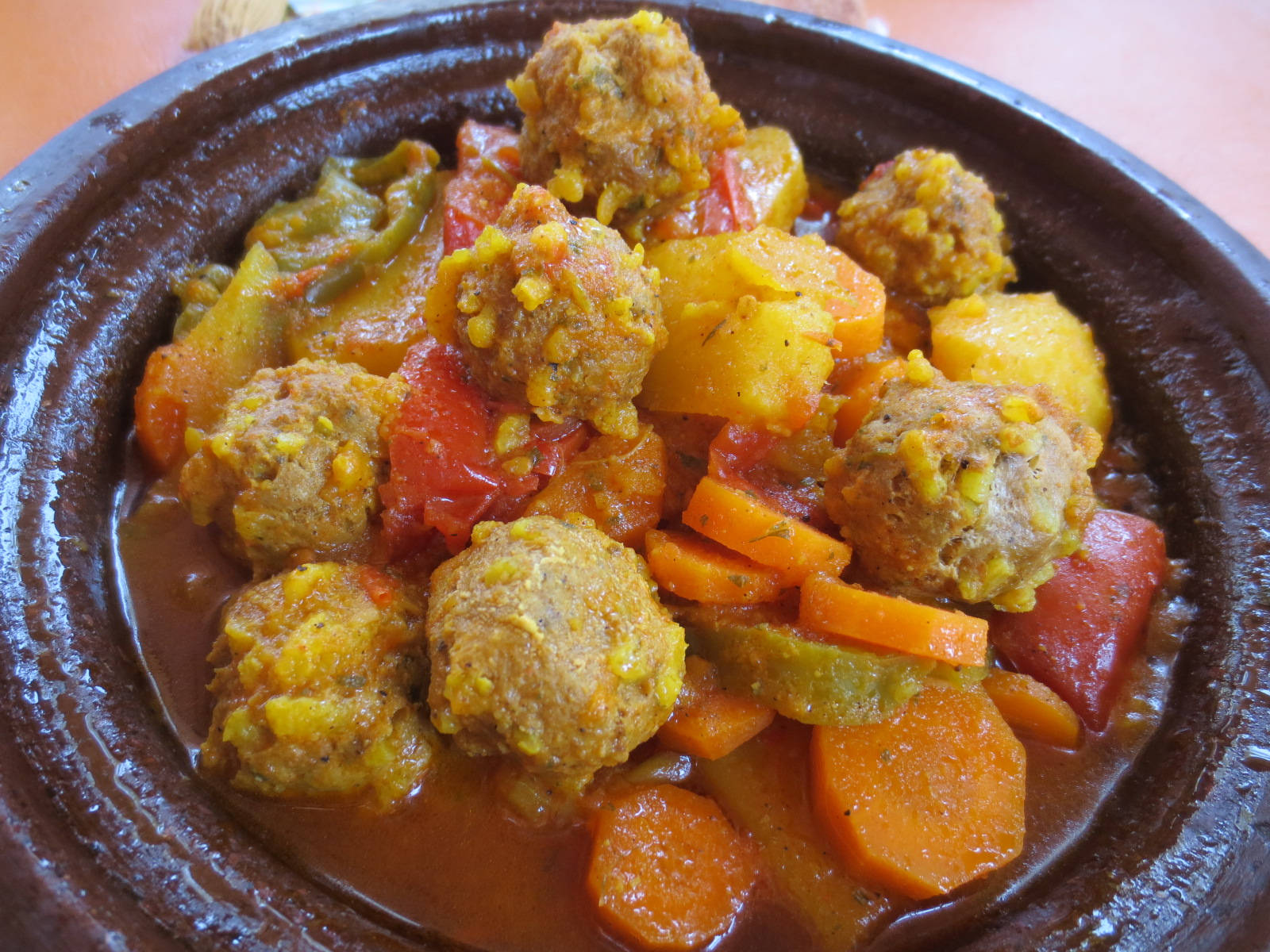 Delicious Food 桌布 壁紙 — 一個質樸的粘土塔吉鍋，盛滿金黃色肉丸和色彩繽紛的蔬菜，配上濃郁醬汁。