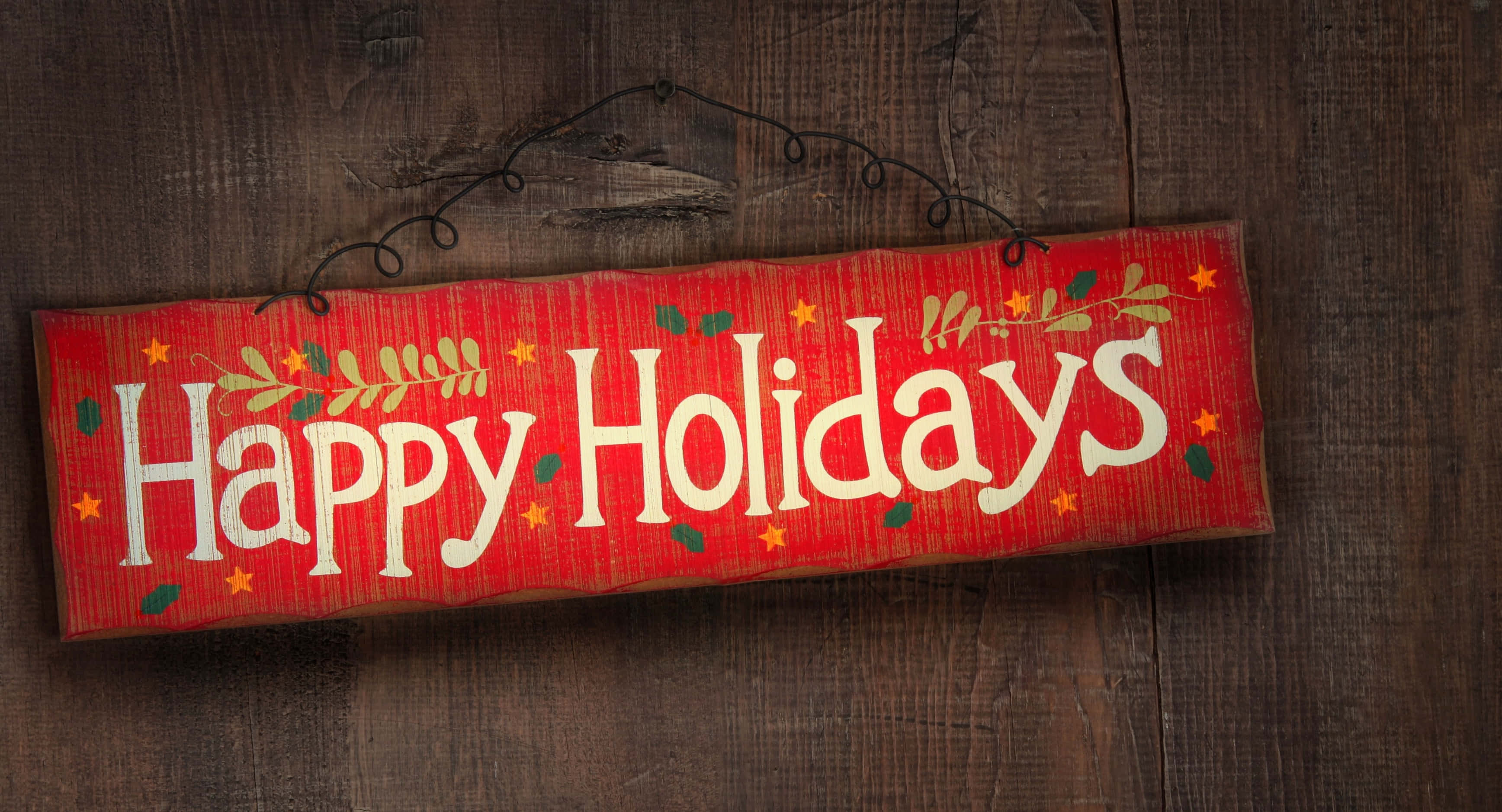 Happy Holidays 桌布 壁紙 — 一個質樸的紅色木製標牌，帶有白色「Happy Holidays」文字和綠色星星，掛在深色木質背景上。