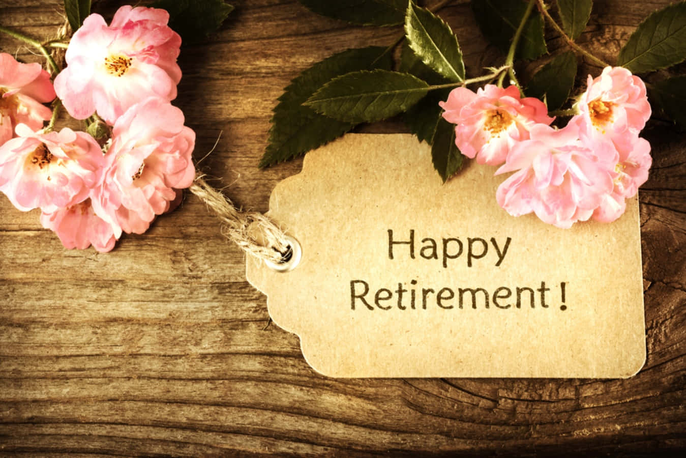 Retirement 桌布 壁紙 — 一個質樸的紙標籤，上面寫著「Happy Retirement!」，周圍環繞著粉紅玫瑰，放在經風化的木質表面上。