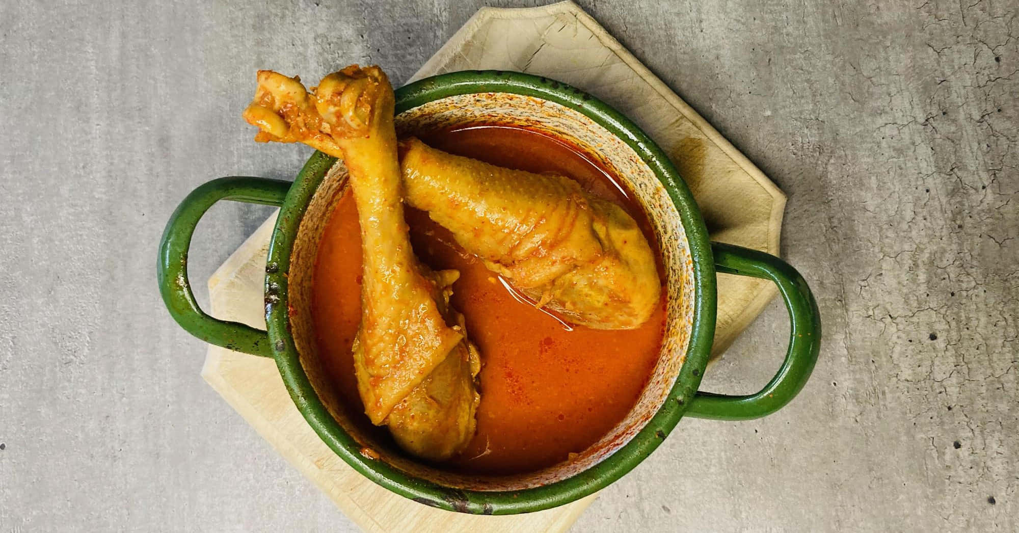 Chicken 桌布 壁紙 — 一個質樸的綠色鍋子盛載著濃郁的橙色雞肉咖哩，兩隻雞腿浸在醬汁中，放在木板上。