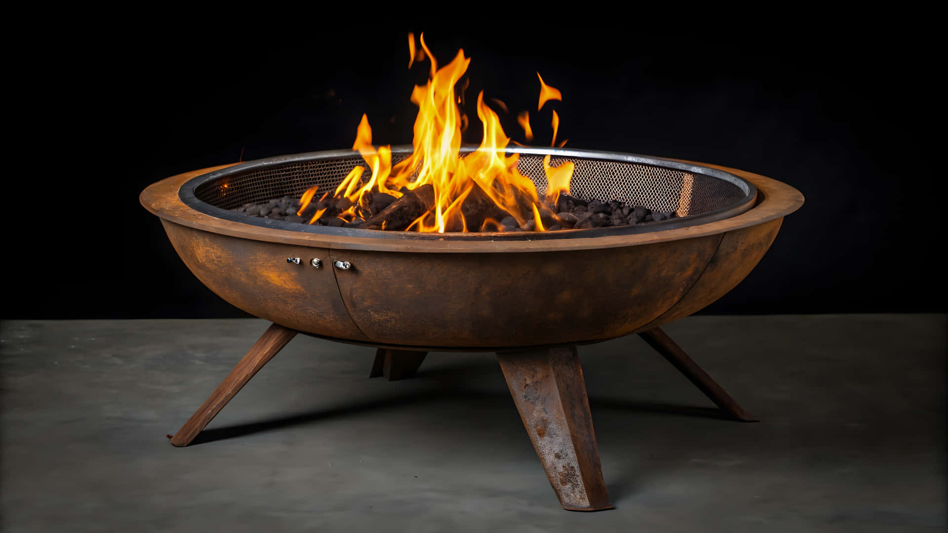Burning fire in a rustic metal fire pit with dark background 壁紙 — 一個質樸的金屬火坑，鮮豔的橙色火焰在黑暗背景下於發光的木炭上舞動。