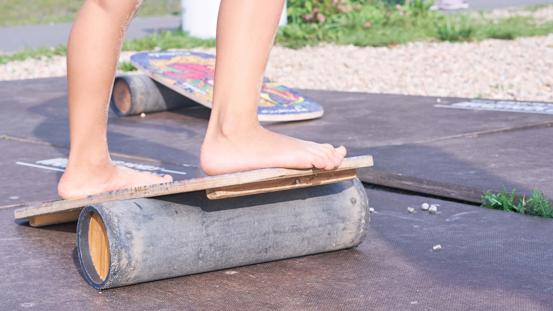Outdoor Activities 桌布 壁紙 — 一個赤腳的人平衡在一塊放在風化木頭上的木板上，地面是一塊深色墊子，在戶外。