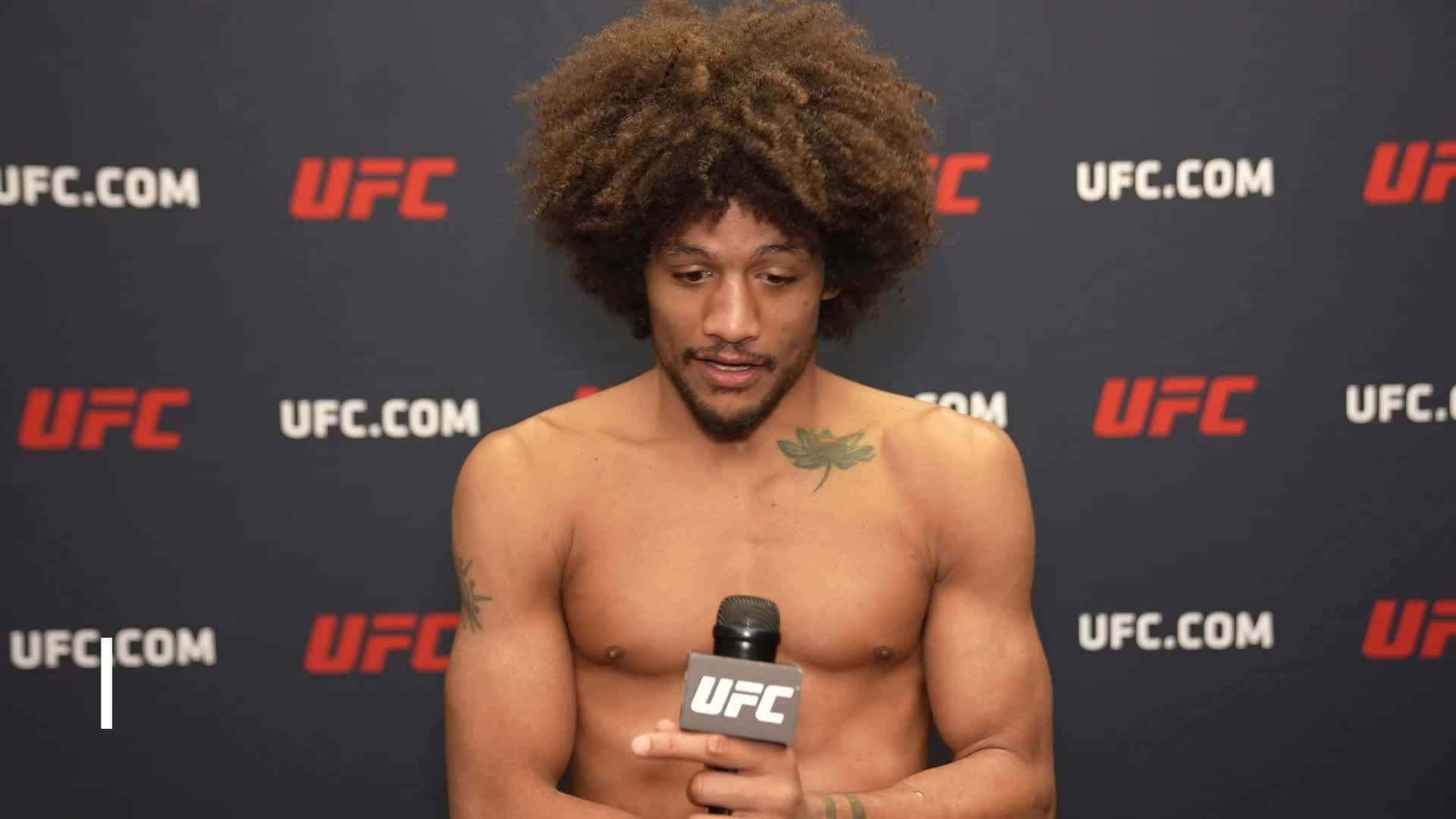 UFC 桌布 壁紙 — 一個赤膊、留著大爆炸頭的拳手，在品牌背景前拿著UFC麥克風。