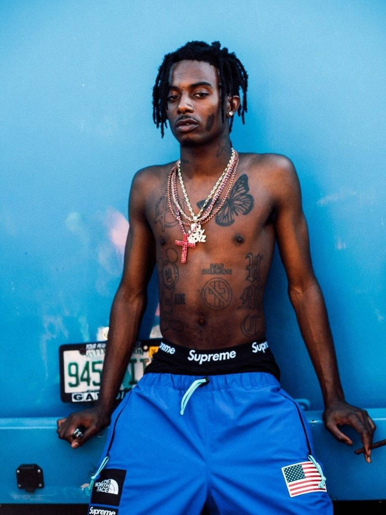 Carti 桌布 壁紙 — 一個赤膊、留著辮子頭、有刺青的男人，穿著Supreme短褲和層疊項鍊，靠在一輛藍色卡車上。