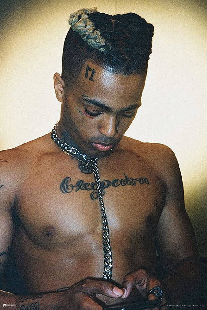 酷酷的xxxtentacion 桌布 壁紙 — 一個赤膊、編髮、有刺青的男人在溫暖燈光的室內環境中低頭看手機。