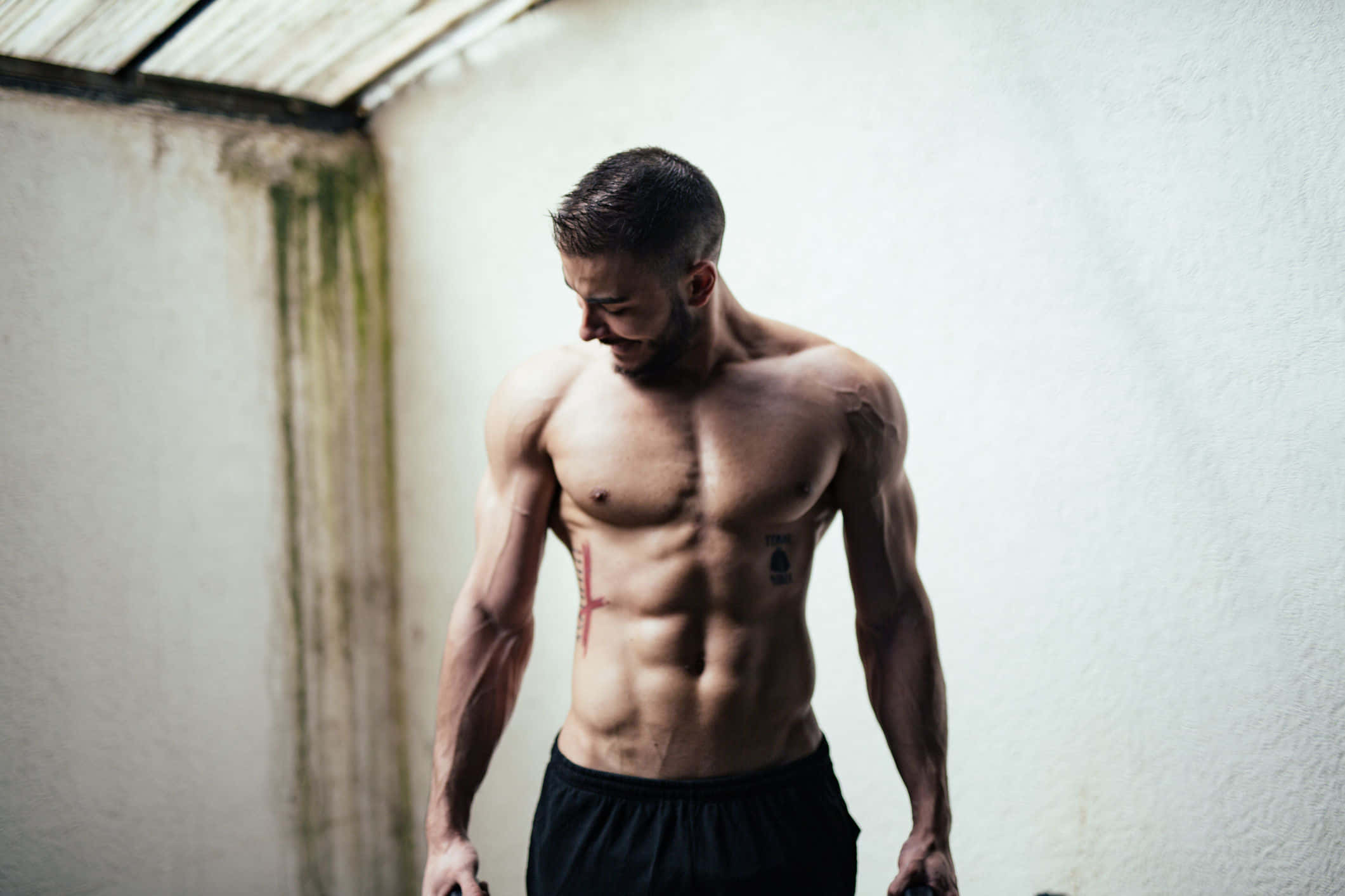 abs 桌布 壁紙 — 一個赤膊、肌肉線條分明的男人站在粗糙的工業空間，低頭，汗水在他的皮膚上閃閃發光。