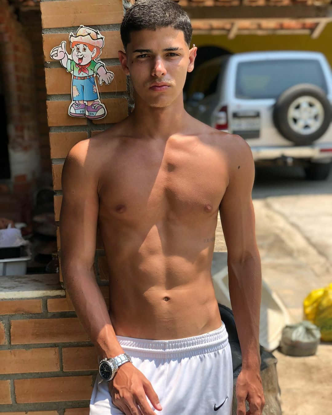 Hot Guy 桌布 壁紙 — 一個赤膊上身、腹肌線條分明的年輕男子，在明亮陽光下自信地靠著磚牆站立。
