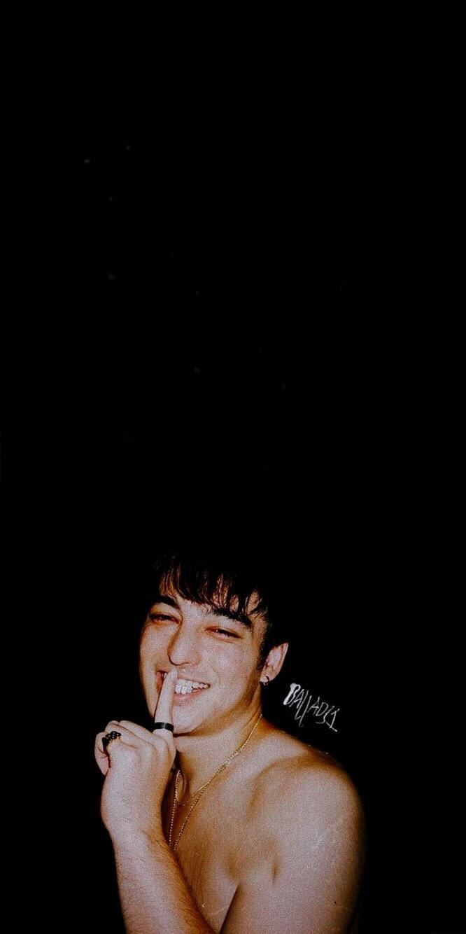 joji 桌布 壁紙 — 一個赤膊的深色頭髮年輕男子在黑色背景前頑皮地咧嘴笑，手指按在嘴唇上。