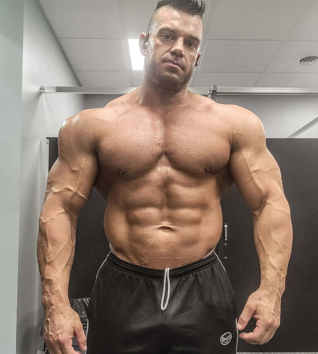 abs 桌布 壁紙 — 一個赤膊肌肉男，擁有明顯腹肌和粗壯手臂，在健身房更衣室自信地擺姿勢。