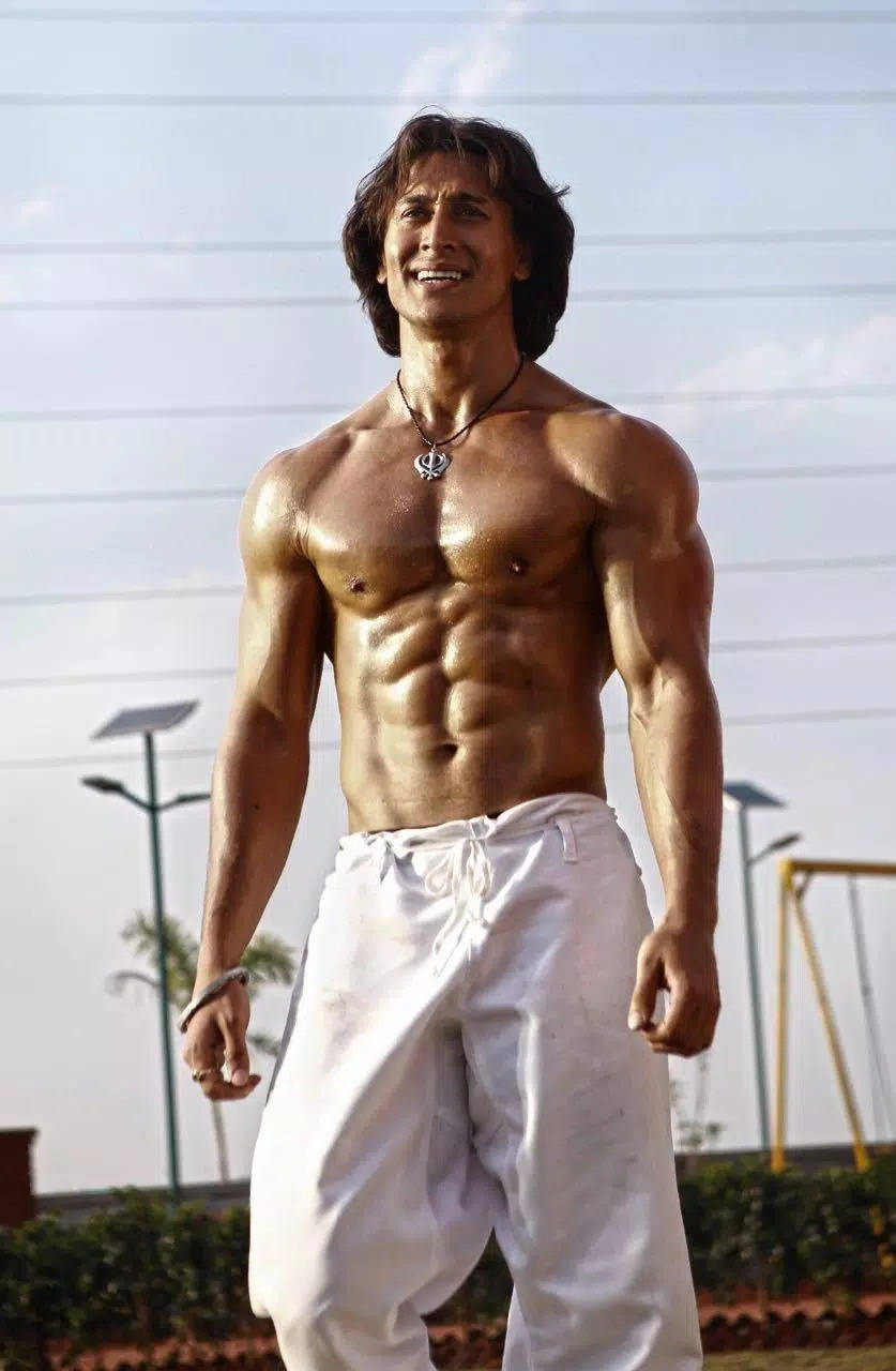 Indian 桌布 壁紙 — 一個赤膊肌肉男，有明顯腹肌和愉快笑容，穿著白色褲子站在戶外明亮日光下。
