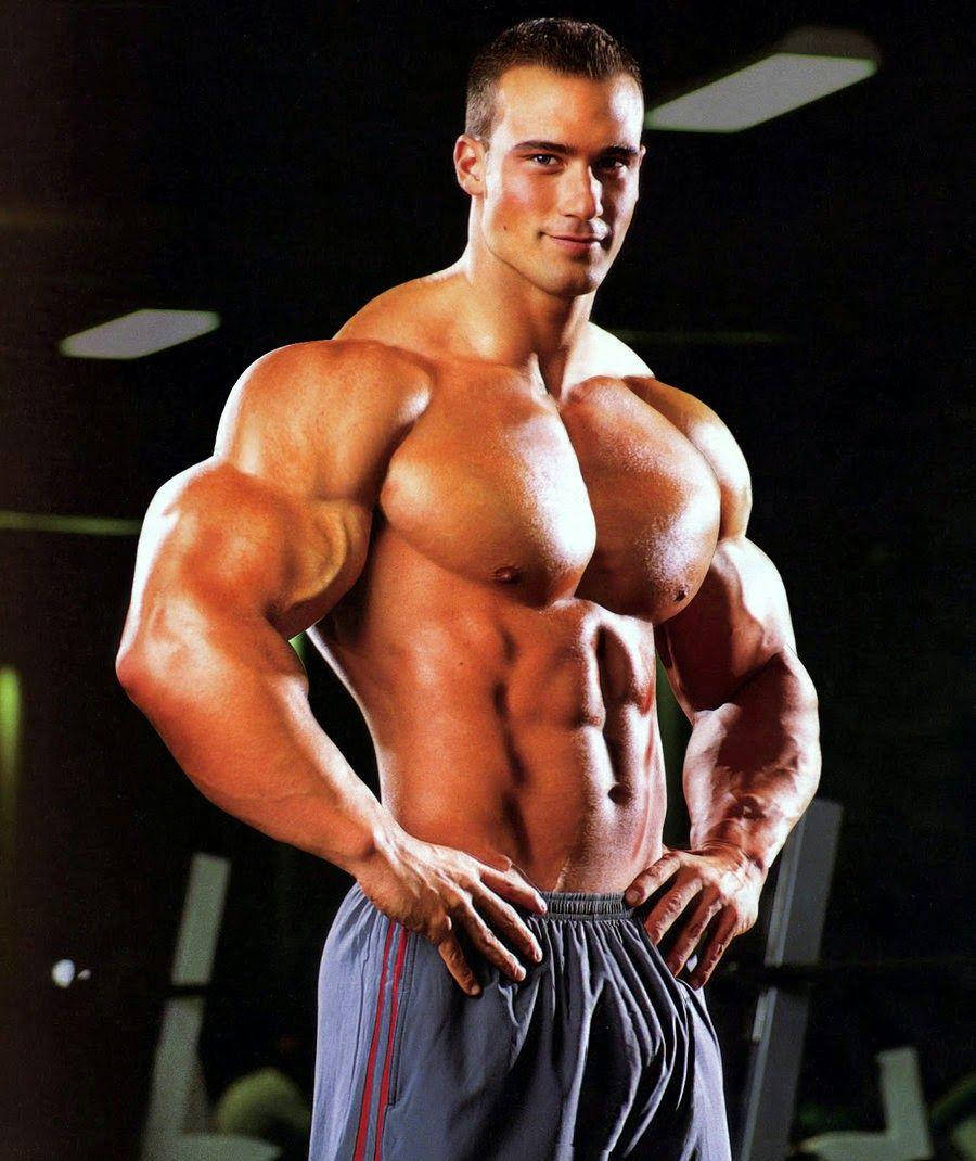 Exercise 桌布 壁紙 — 一個赤膊肌肉男，腹肌和手臂線條分明，在燈光昏暗的健身房自信地叉腰擺姿勢。