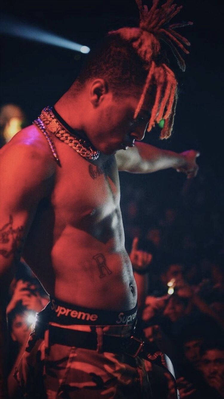 xxxtentacion 美學 桌布 壁紙 — 一個赤裸上身、留著雷鬼辮和刺青的男人，在紅色燈光下，身後有群眾，在舞台上表演。