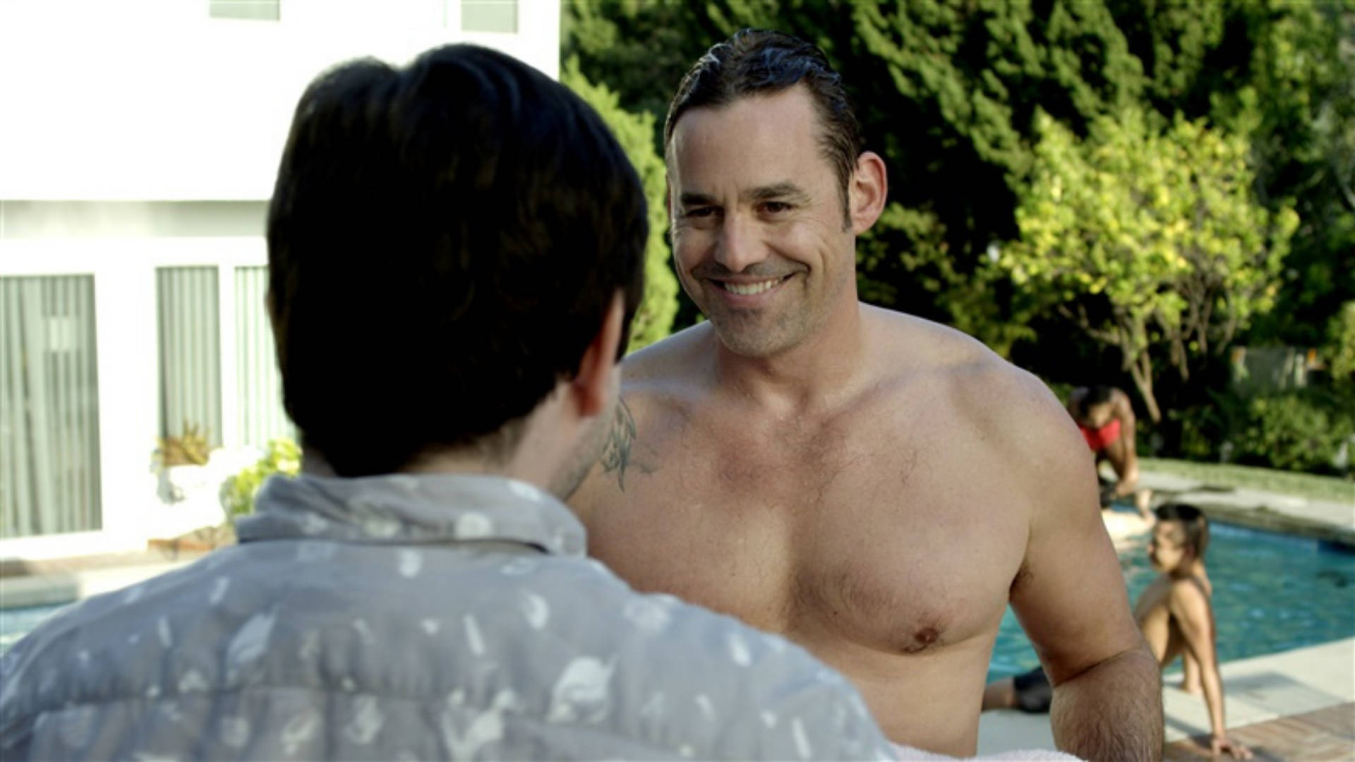Nicholas Brendon 桌布 壁紙 — 一個赤裸上身的刺青男子在陽光普照的游泳池旁，被茂密的綠植環繞，對另一個人溫暖地微笑。