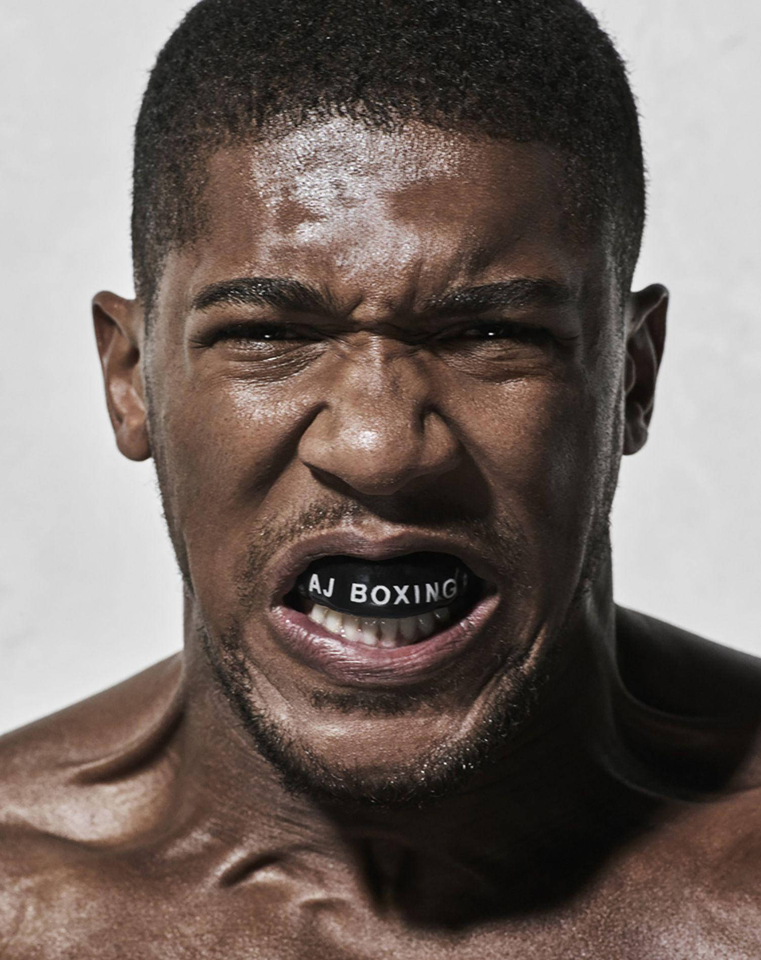 Anthony Joshua 桌布 壁紙 — 一個赤裸上身的拳擊手，帶著強烈的專注力咆哮，汗水在他臉上閃閃發光，而 'AJ BOXING' 文字在他的牙齒中發光。