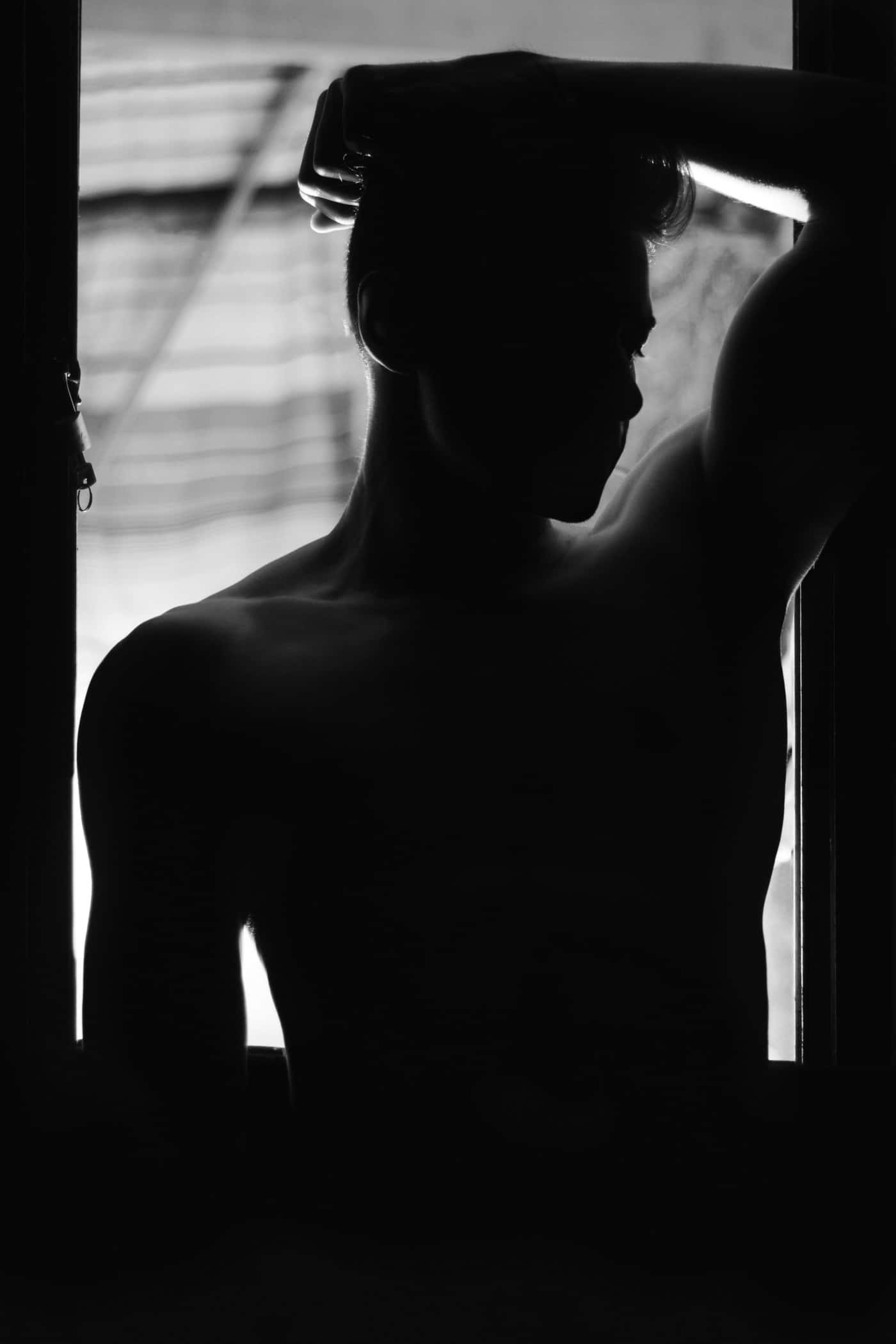 Silhouette 桌布 壁紙 — 一個赤裸上身的男人剪影站在窗邊，背光被明亮的光線照射，手舉到頭上，呈現沉思姿態。