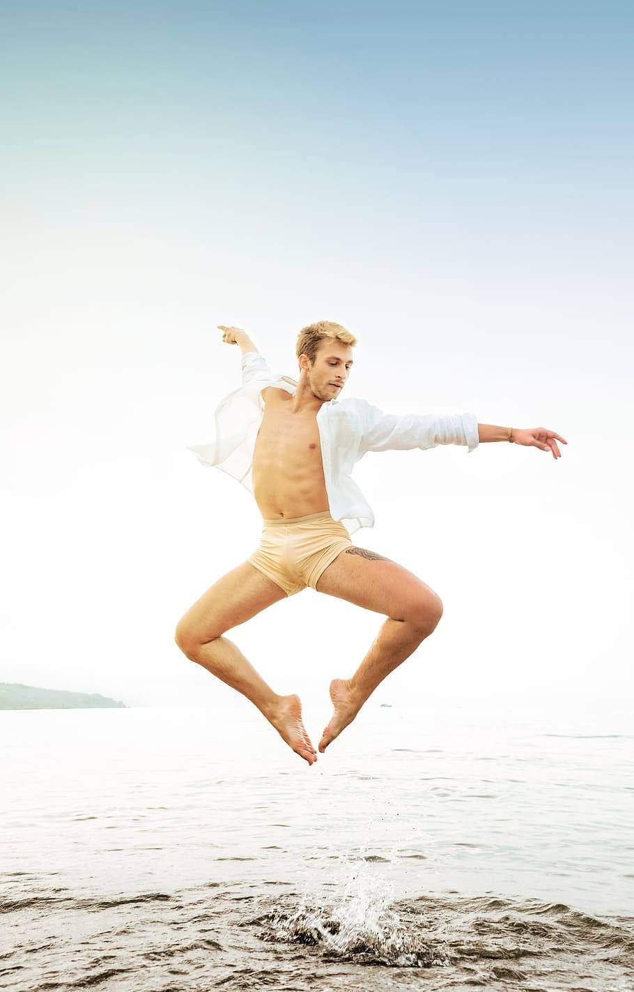 dancer 桌布 壁紙 — 一個赤裸上身的男人在淺水上歡樂地跳躍，雙臂伸展開來，映襯著明亮的天空。