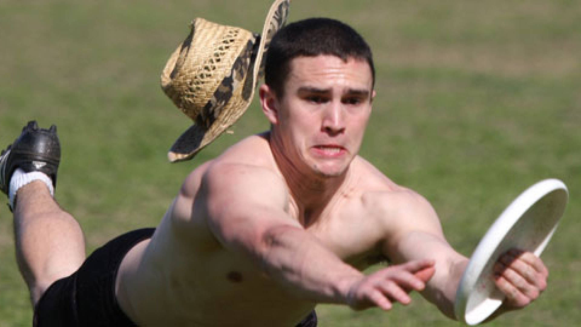 Ultimate Frisbee 桌布 壁紙 — 一個赤裸上身的男人在草地上飛身撲向一個白色飛盤，草帽從他頭上飛走。
