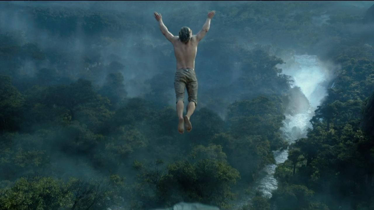 tarzan 桌布 壁紙 — 一個赤裸上身的男人從懸崖上歡快地跳進一個霧氣瀰漫的叢林山谷，下方有瀑布傾瀉而下。